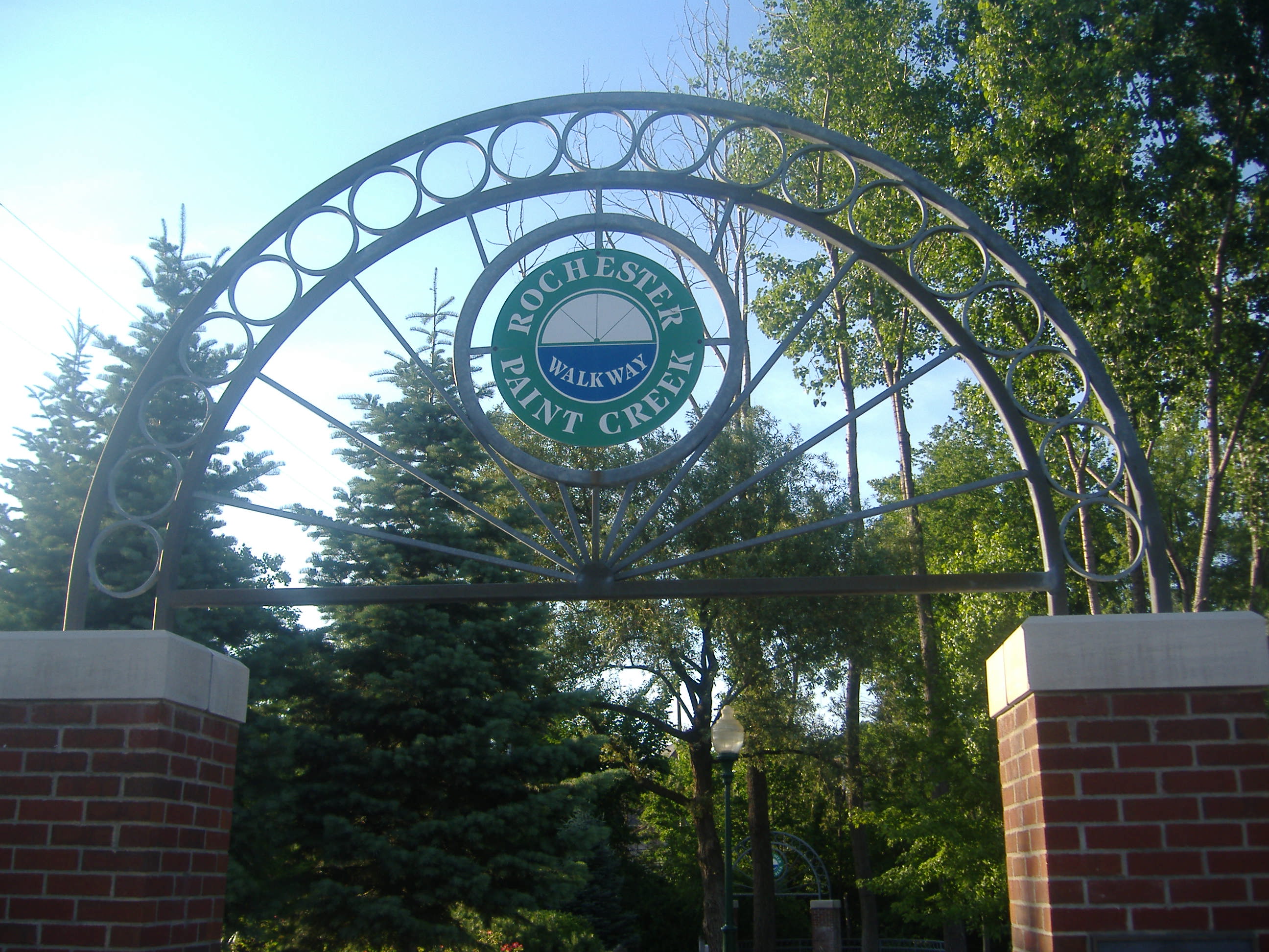 Decorative metal arch entrance to a walking trail, flanked by brick pillars.