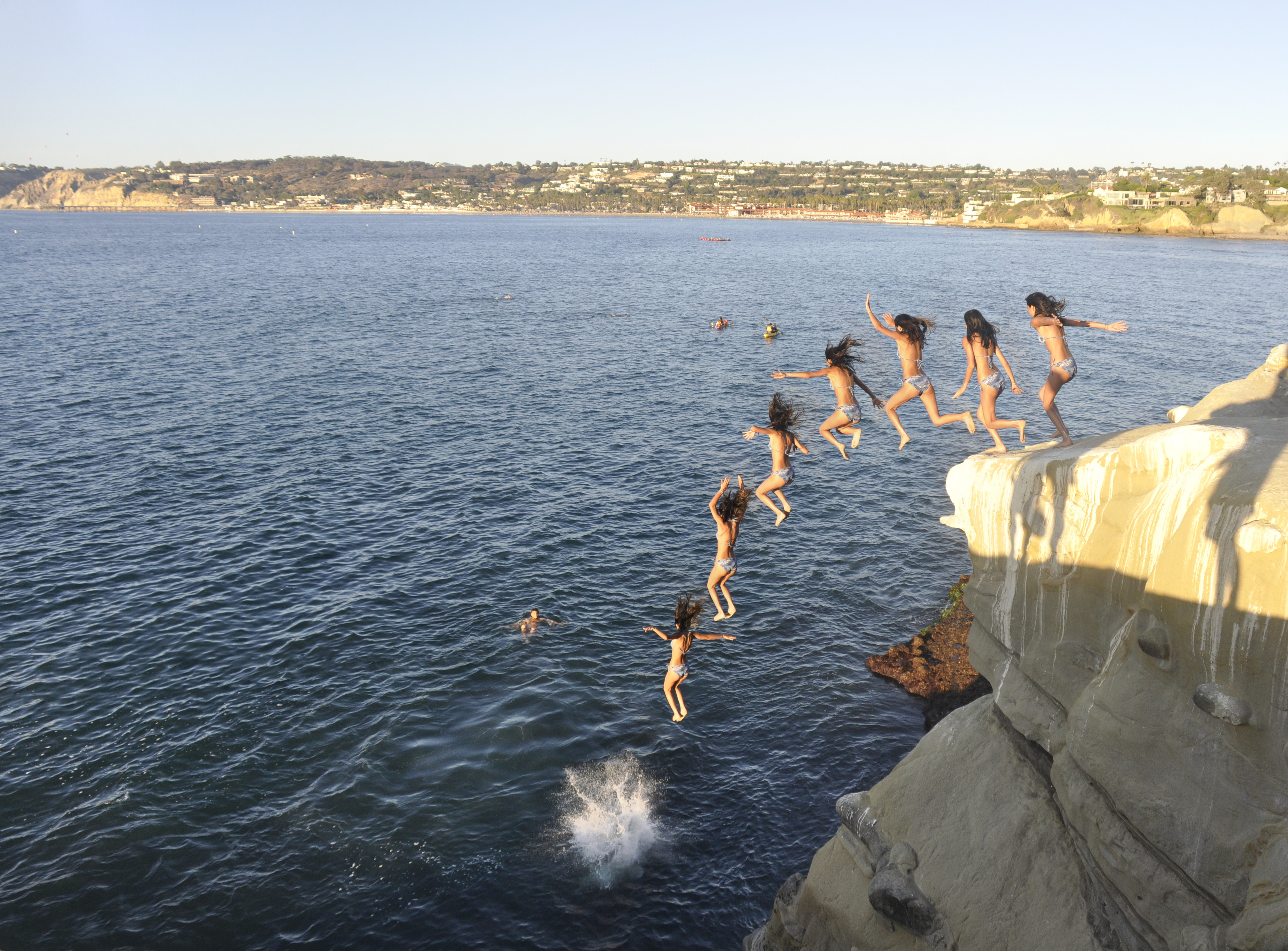 People leaping off a rocky cliff into the ocean near La Jolla Cove.
