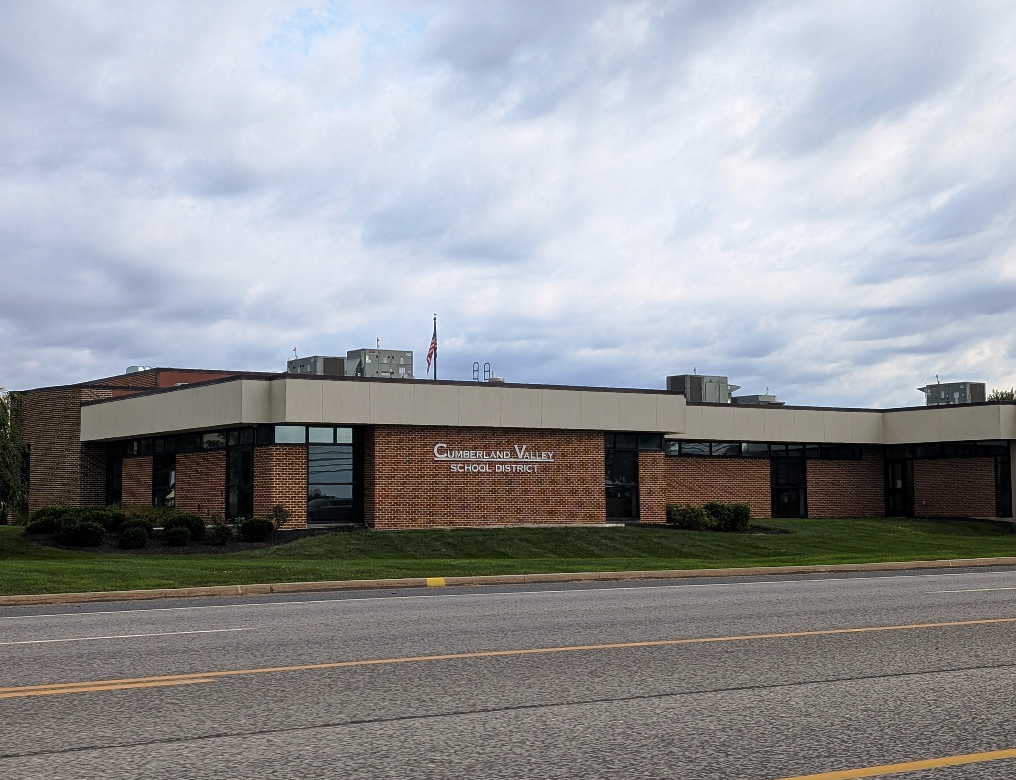 Single-story brick school district office building with a flagpole and manicured lawn.