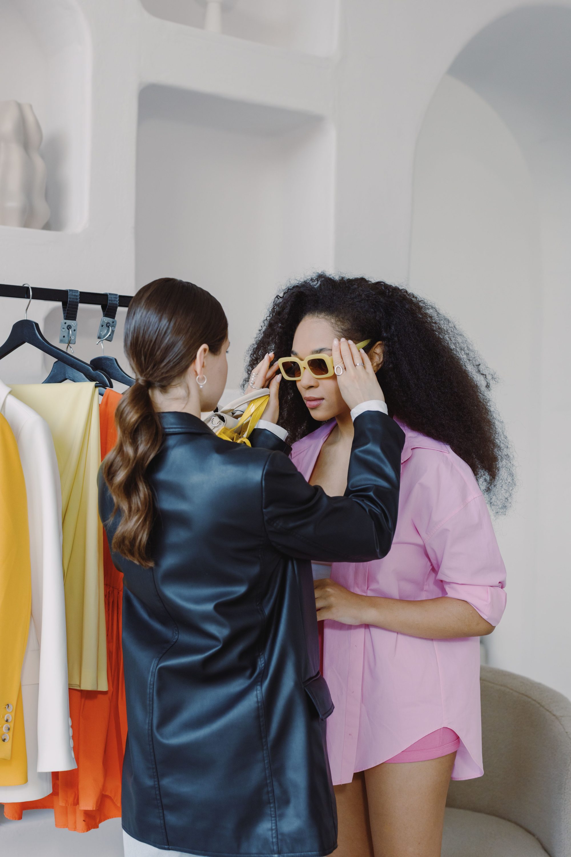 Personal stylist helps client choose sunglasses and outfit in fitting room.