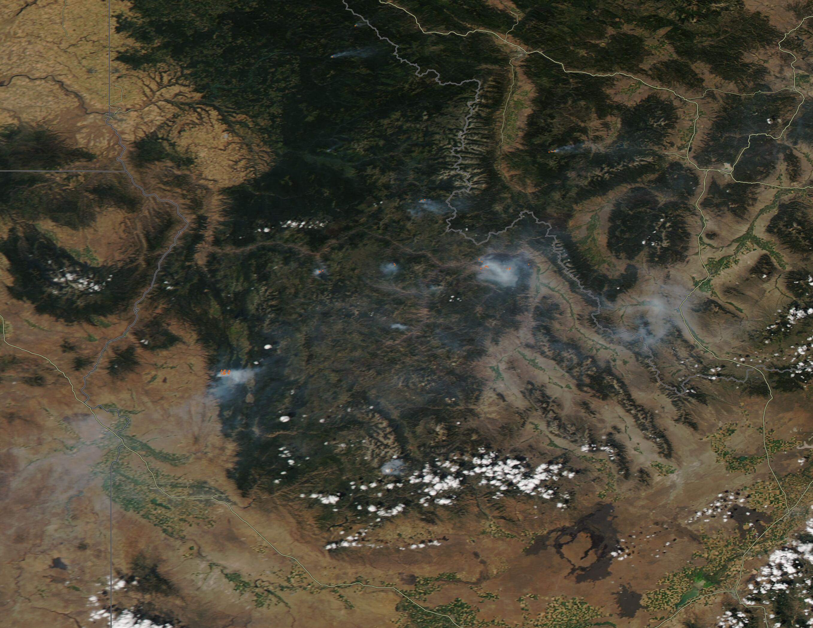 Satellite view showing multiple red wildfire hotspots and smoke plumes over forested land.