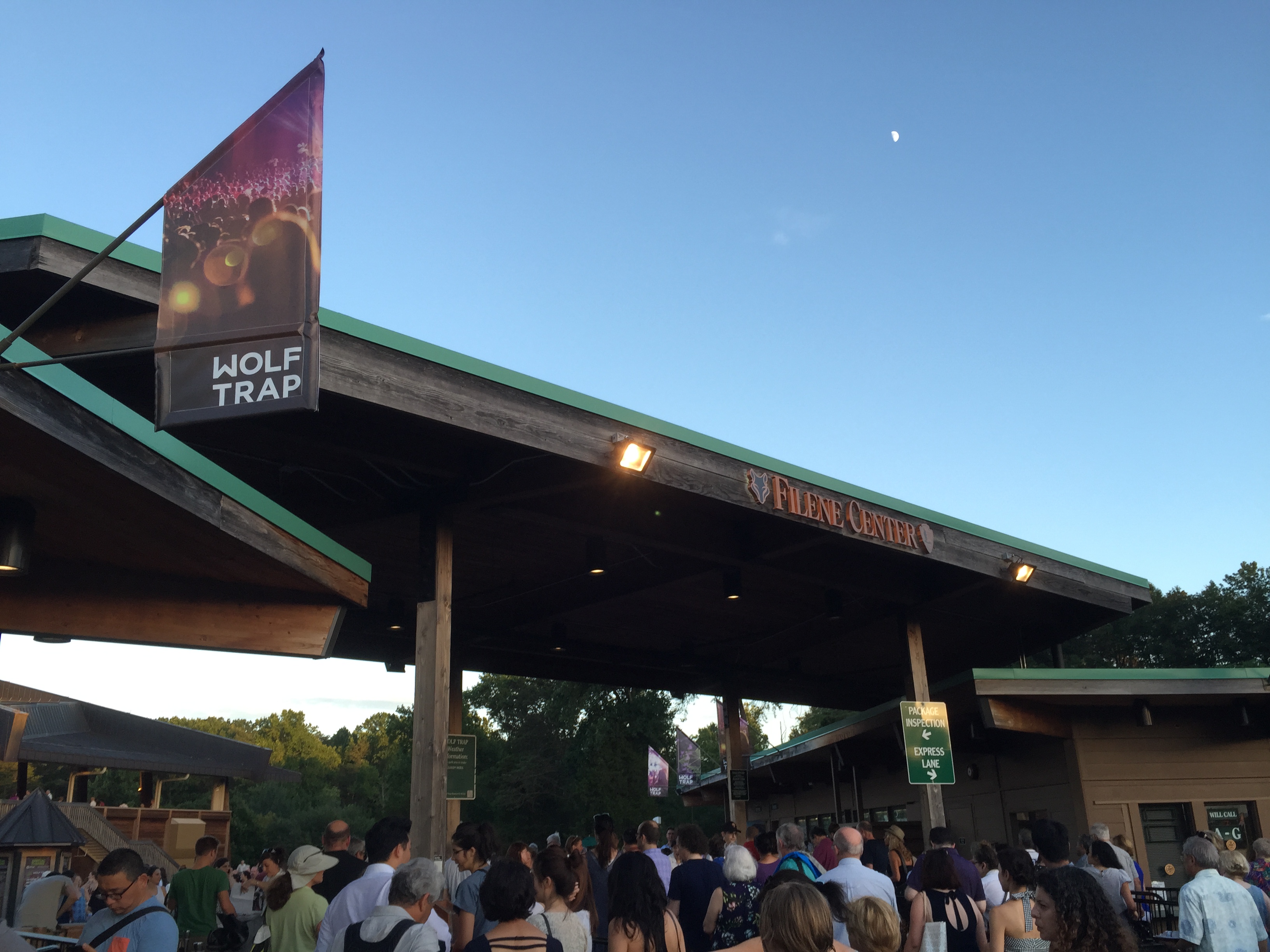 Crowd of people at the entrance to an outdoor performing arts venue at dusk.