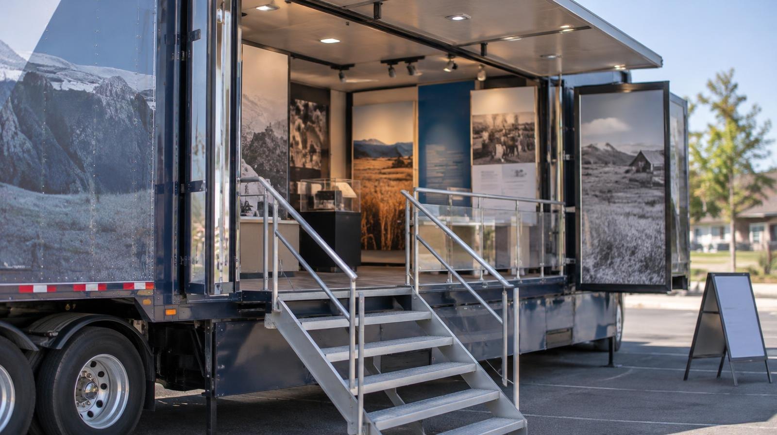 Large tractor-trailer with open side panels revealing an indoor exhibit space.