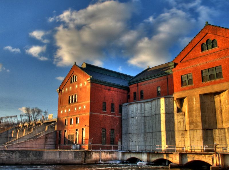 Red-brick hydroelectric powerhouse and concrete dam with flood gates on a river.