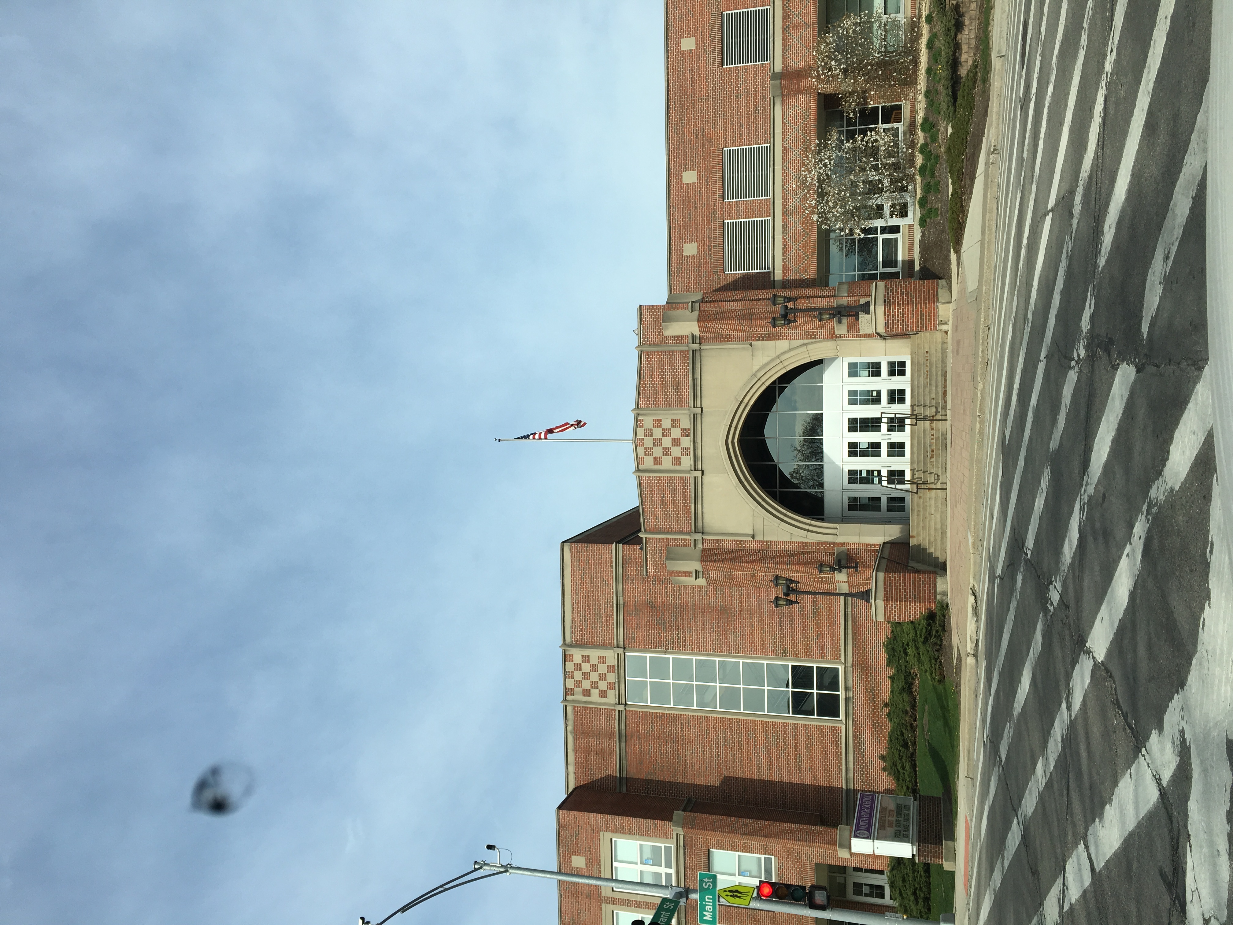 Red brick high school building with arched entrance and American flag on a flagpole.