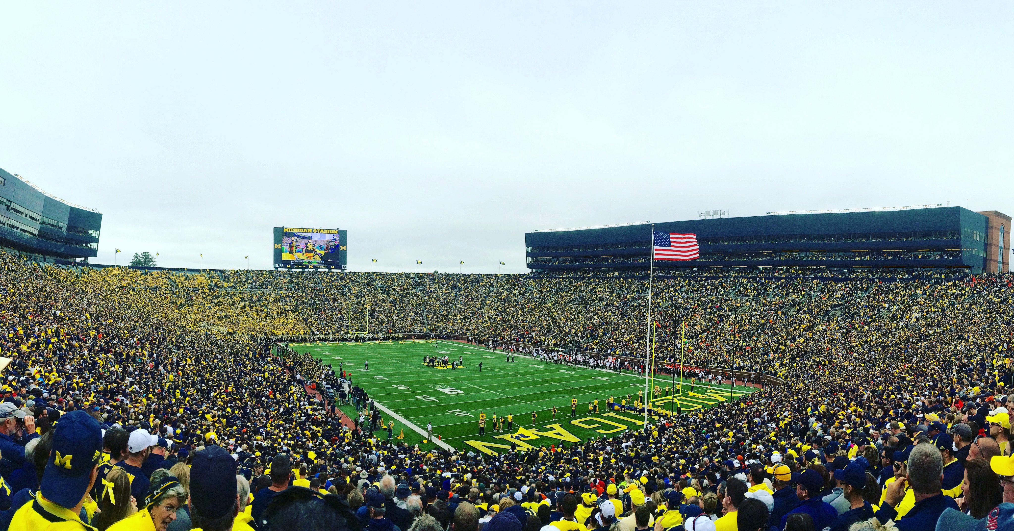 Packed football stadium with maize and blue fans filling the stands around a green field.