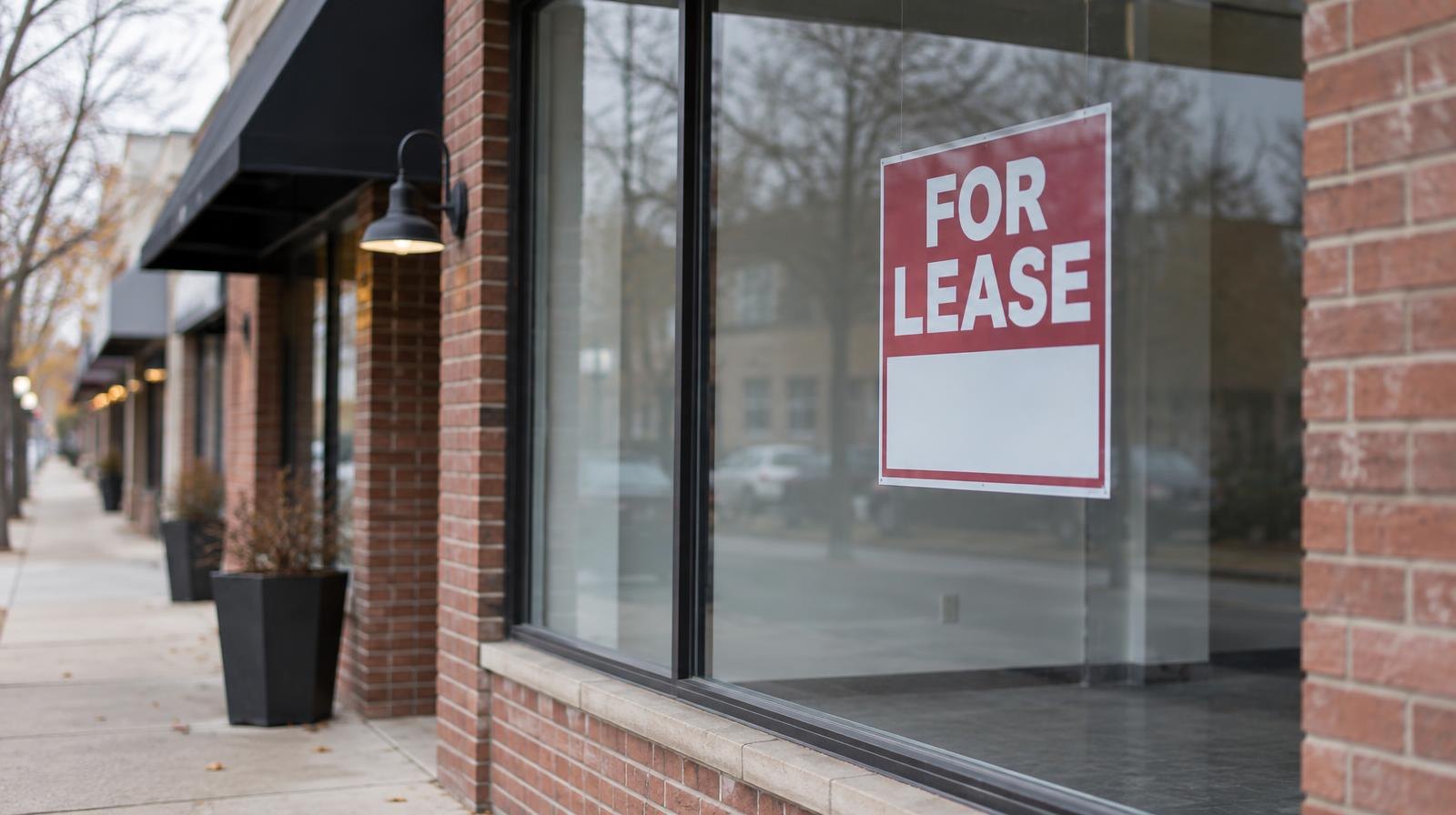 Empty retail storefront with blank display window and a for-lease sign.