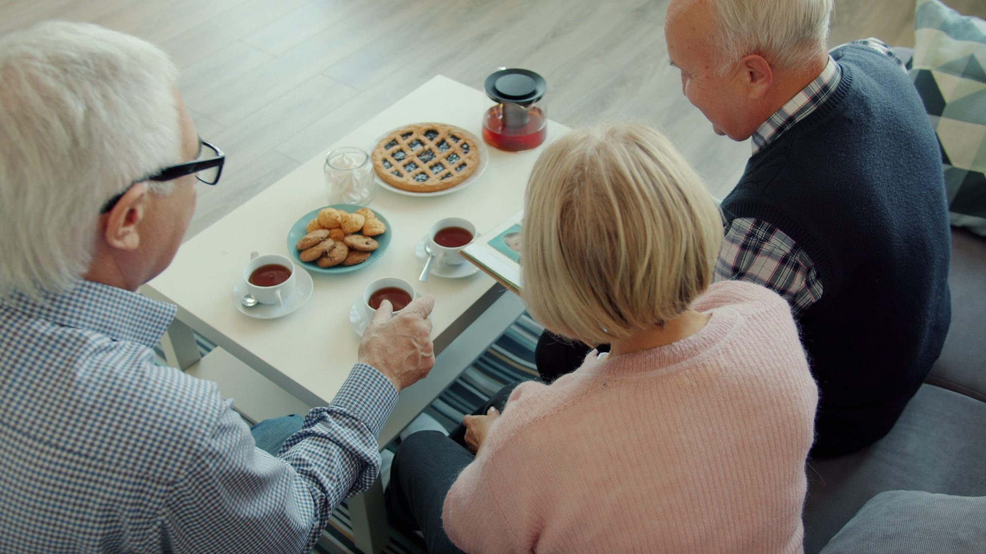 Senior friends gather for tea and cookies in a cozy setting.