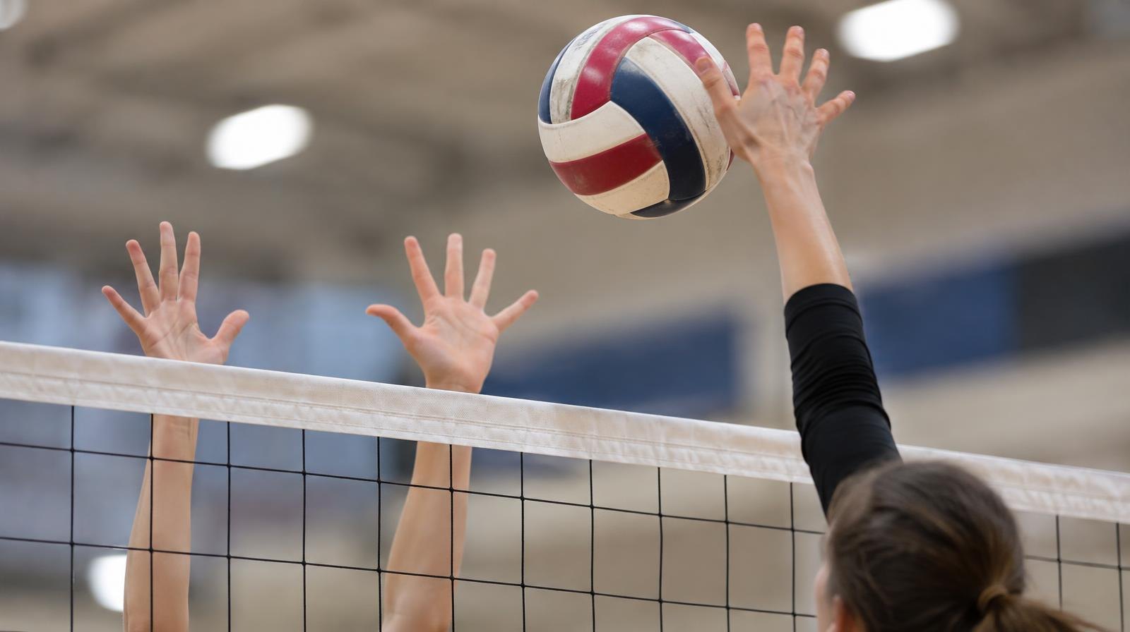 A hand spiking a volleyball over a net in an indoor gym.