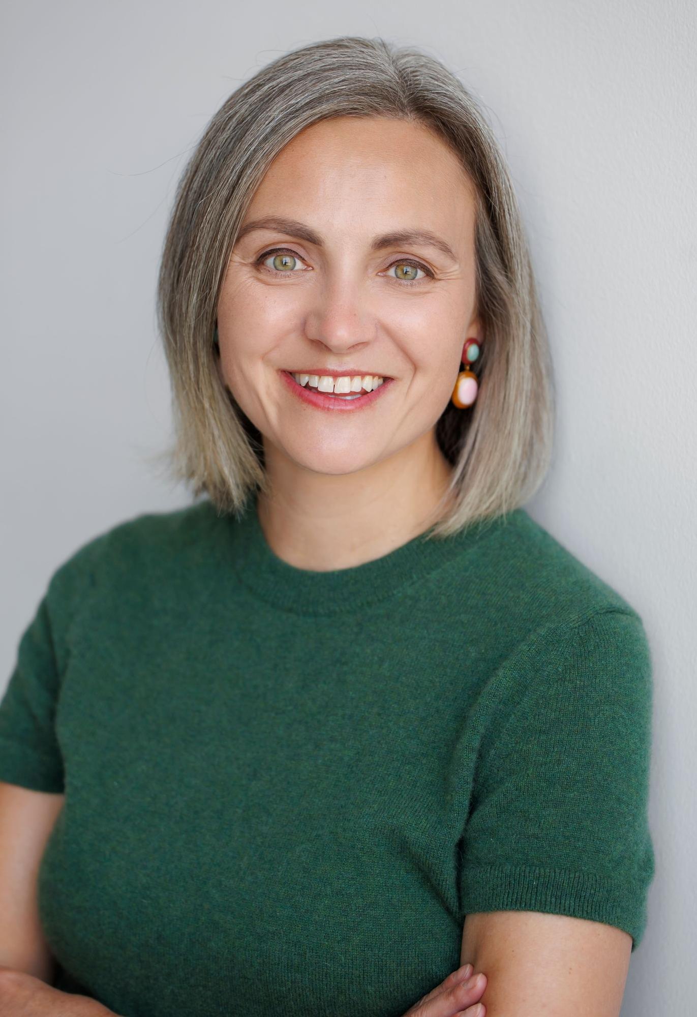 Woman with short gray-streaked hair smiling, arms crossed, against a gray background.