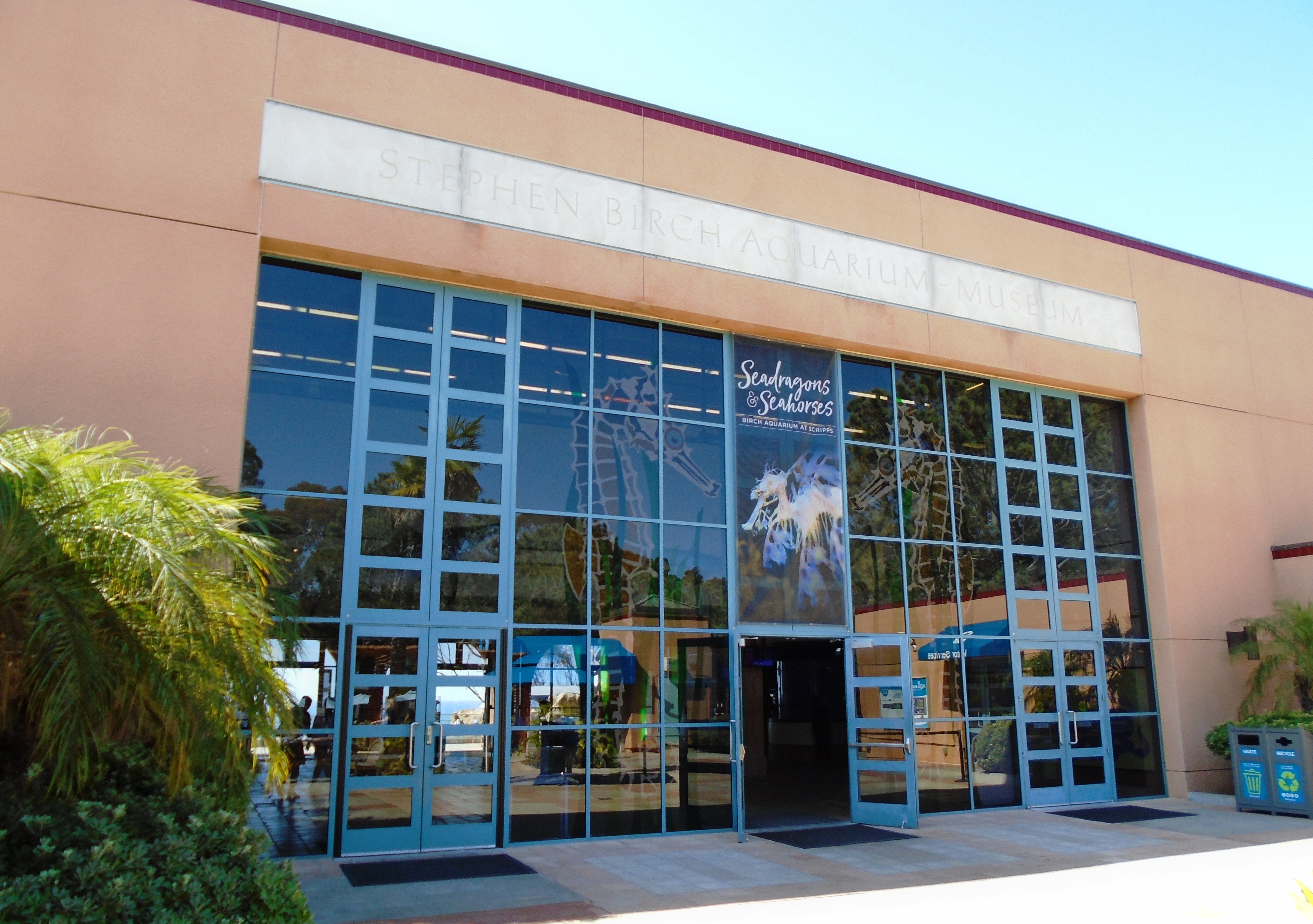 Glass entrance doors of the Stephen Birch Aquarium flanked by palm trees.
