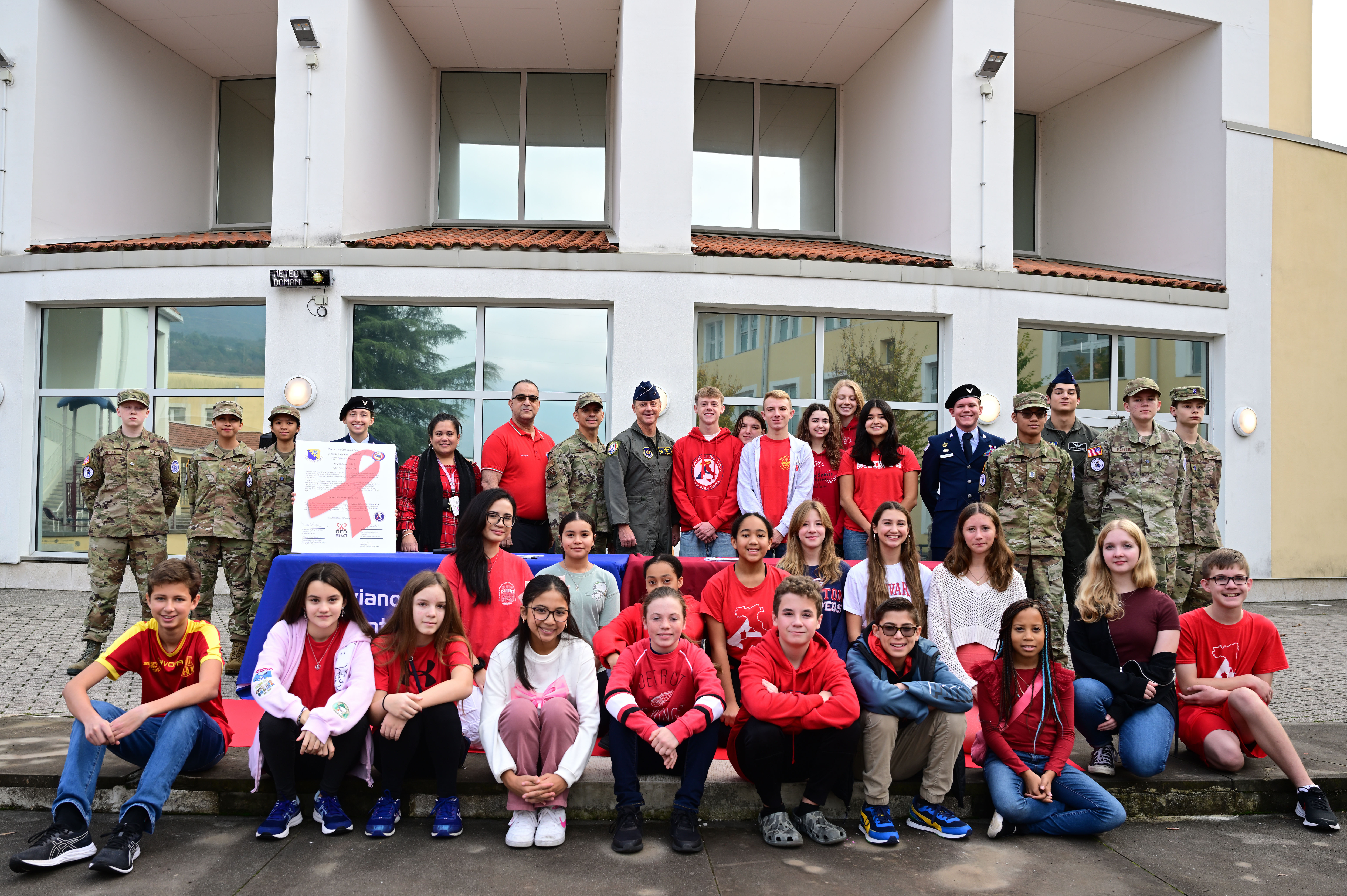 A large group of students and adults pose outdoors holding a Red Ribbon Week banner.