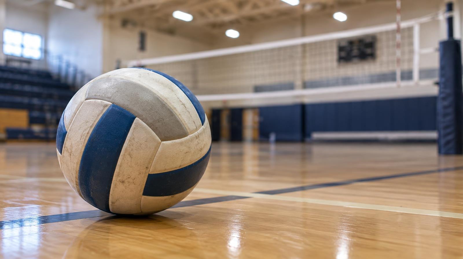 A volleyball resting on a hardwood gymnasium floor near a net.