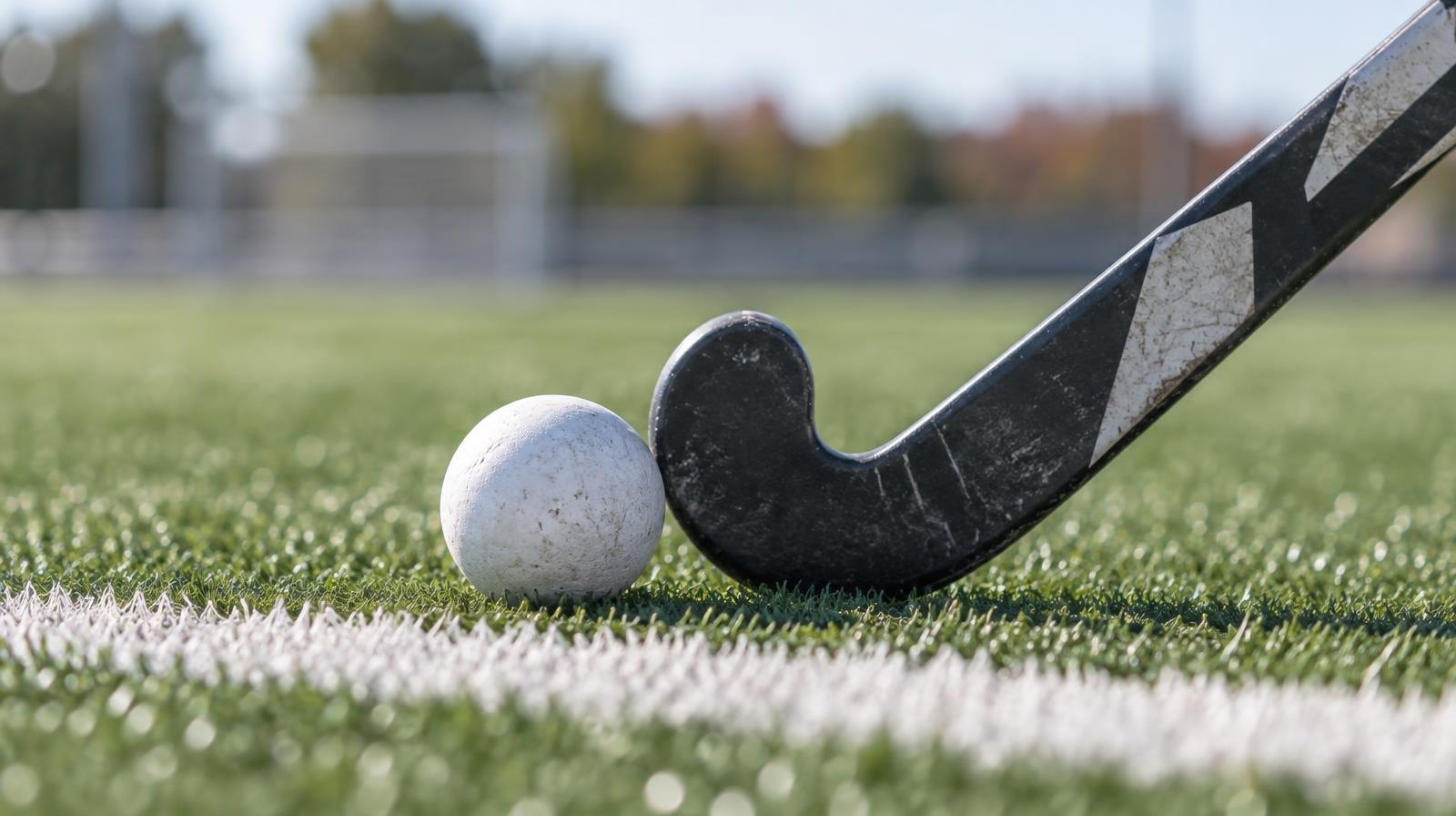 A field hockey stick and ball resting on green artificial turf beside a white line.