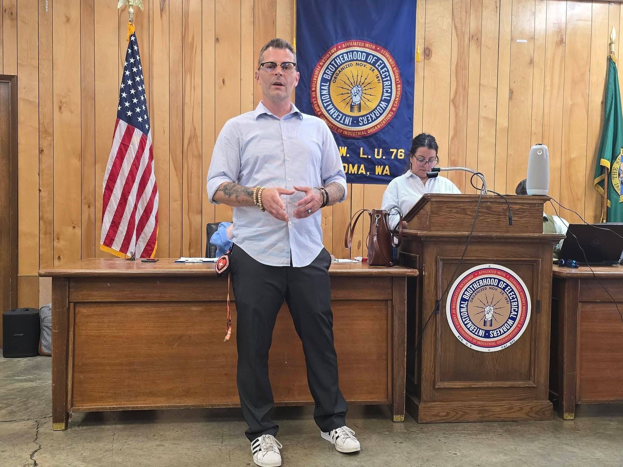 A man speaking at a podium in a union hall with an American flag and union banner behind him.