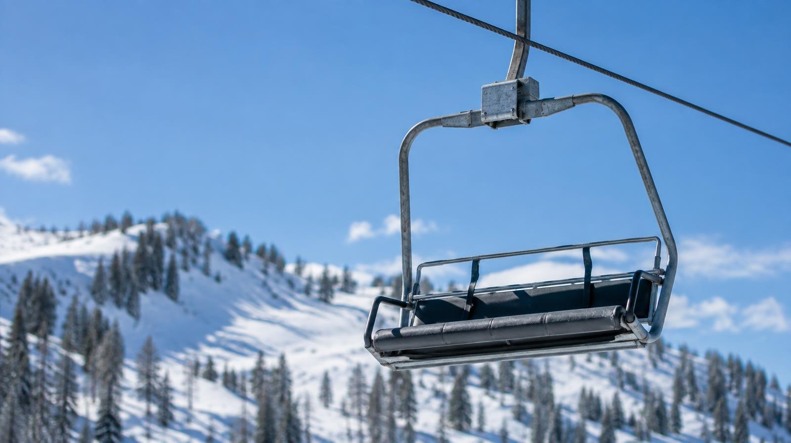 A ski lift chair suspended from a cable above a snowy mountain slope.