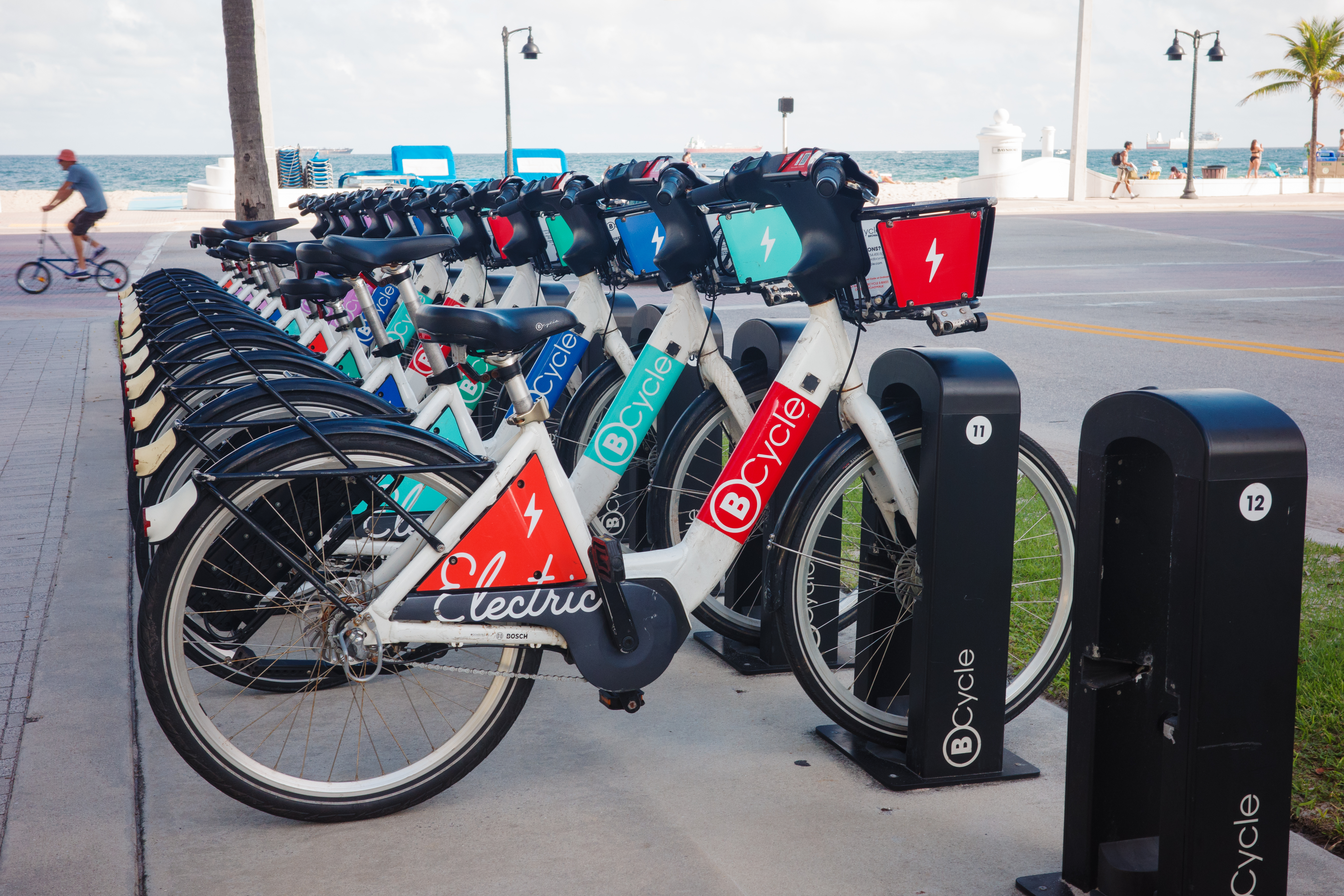 A row of electric bicycles docked at a beachside station near the water.