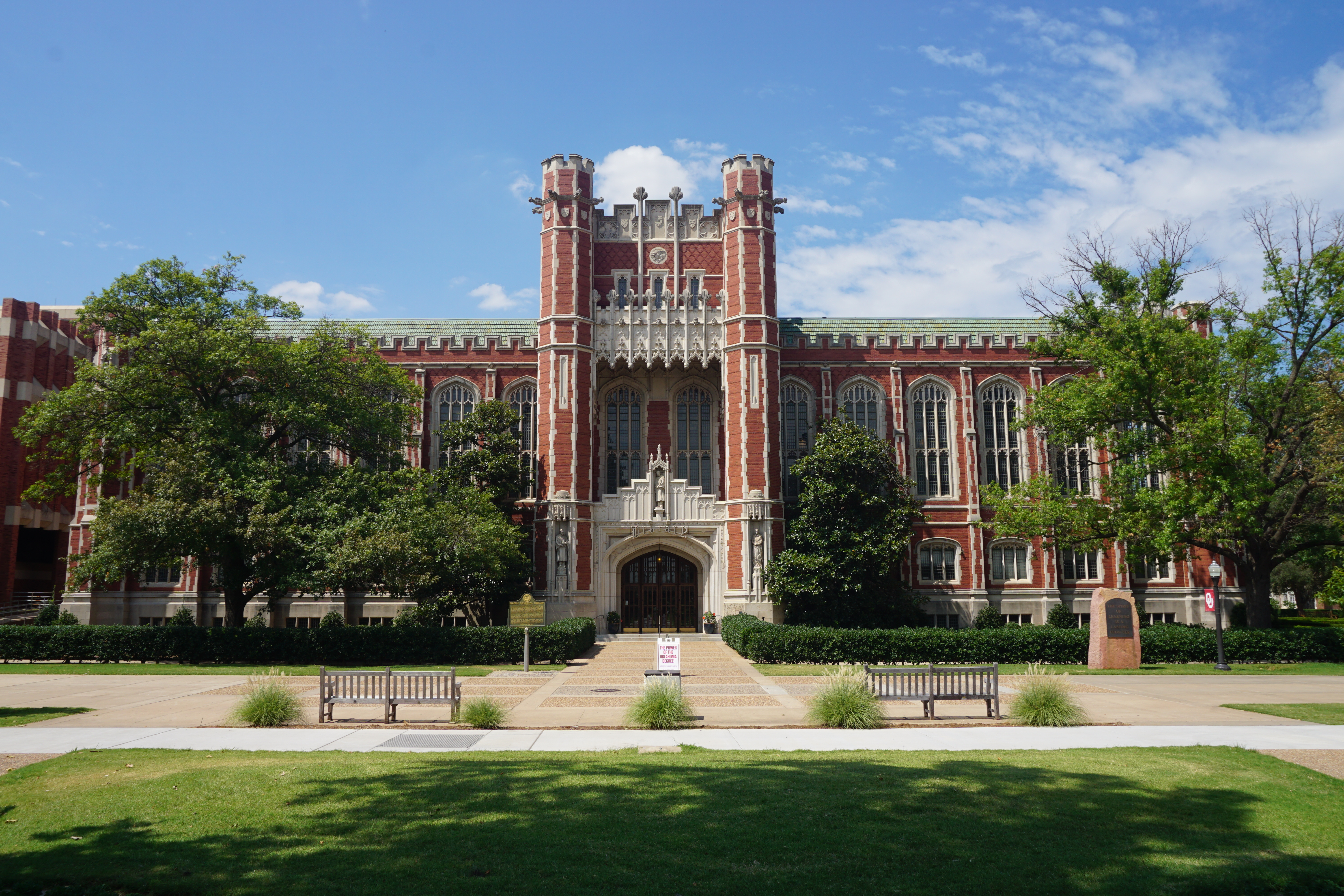 Large red-brick Gothic Revival library building with a central tower on a sunny campus lawn.