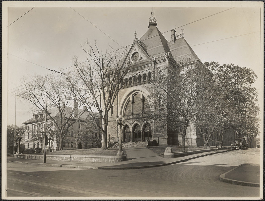 Historic stone municipal building with arched entrances and steep gabled roof on a street corner.