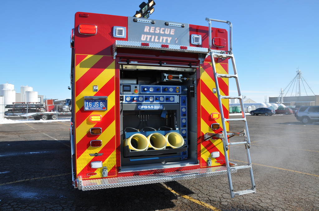 Rear view of a red fire department rescue utility truck with open equipment compartment and chevron striping.