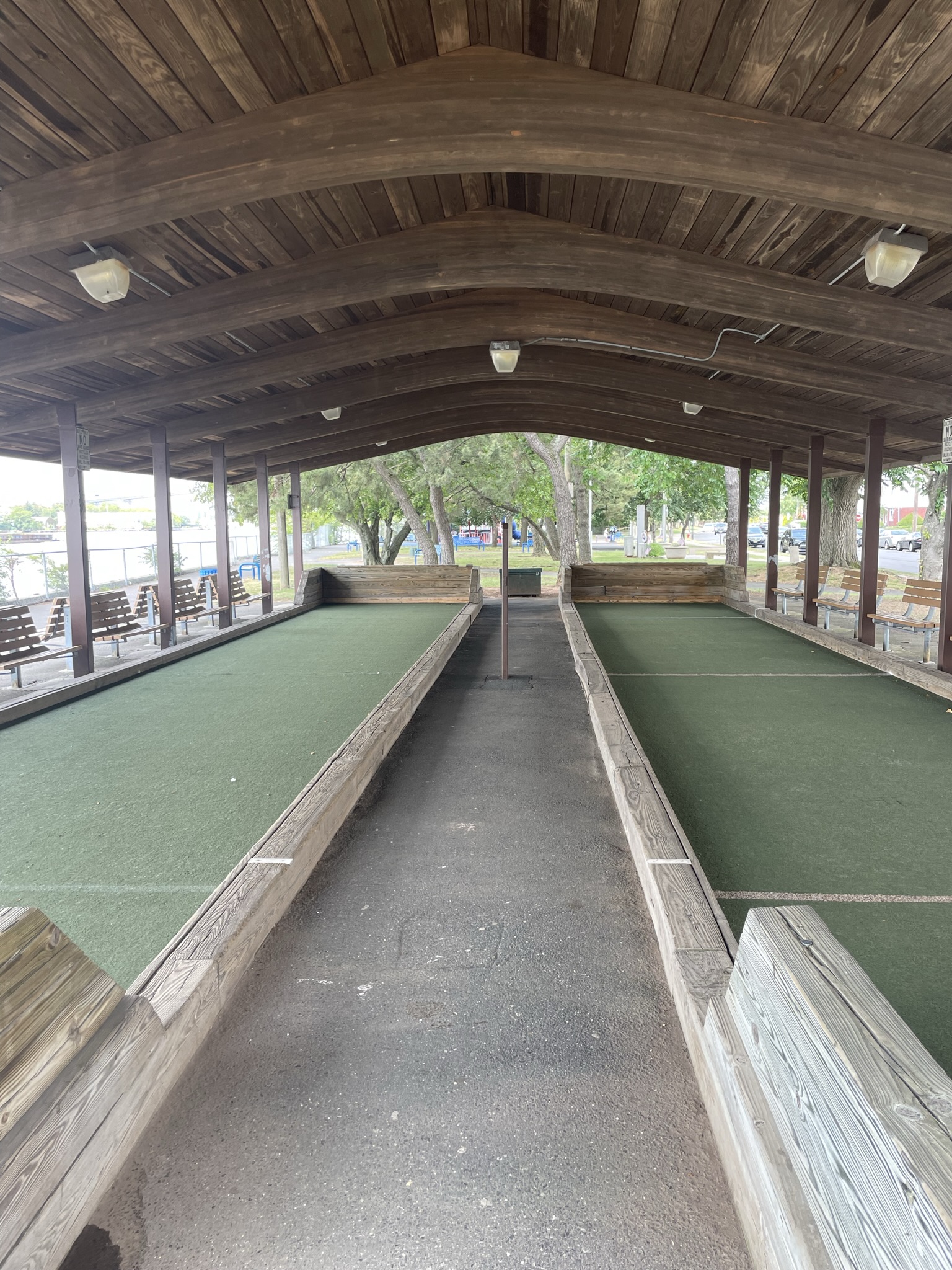 Covered bocce court with green lanes under a curved wooden roof.