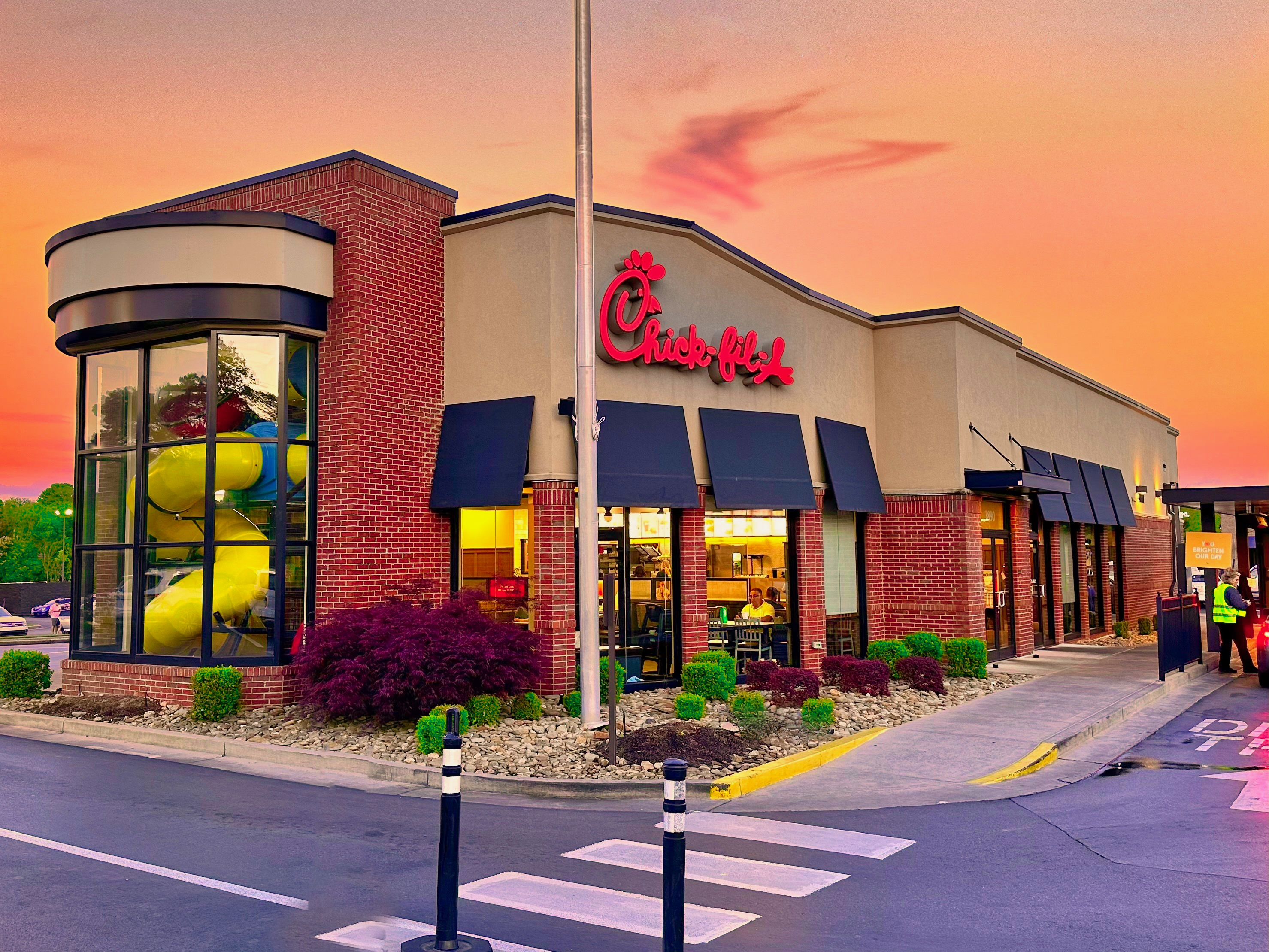 Exterior of a Chick-fil-A restaurant at dusk with brick facade, navy awnings, and lit interior.