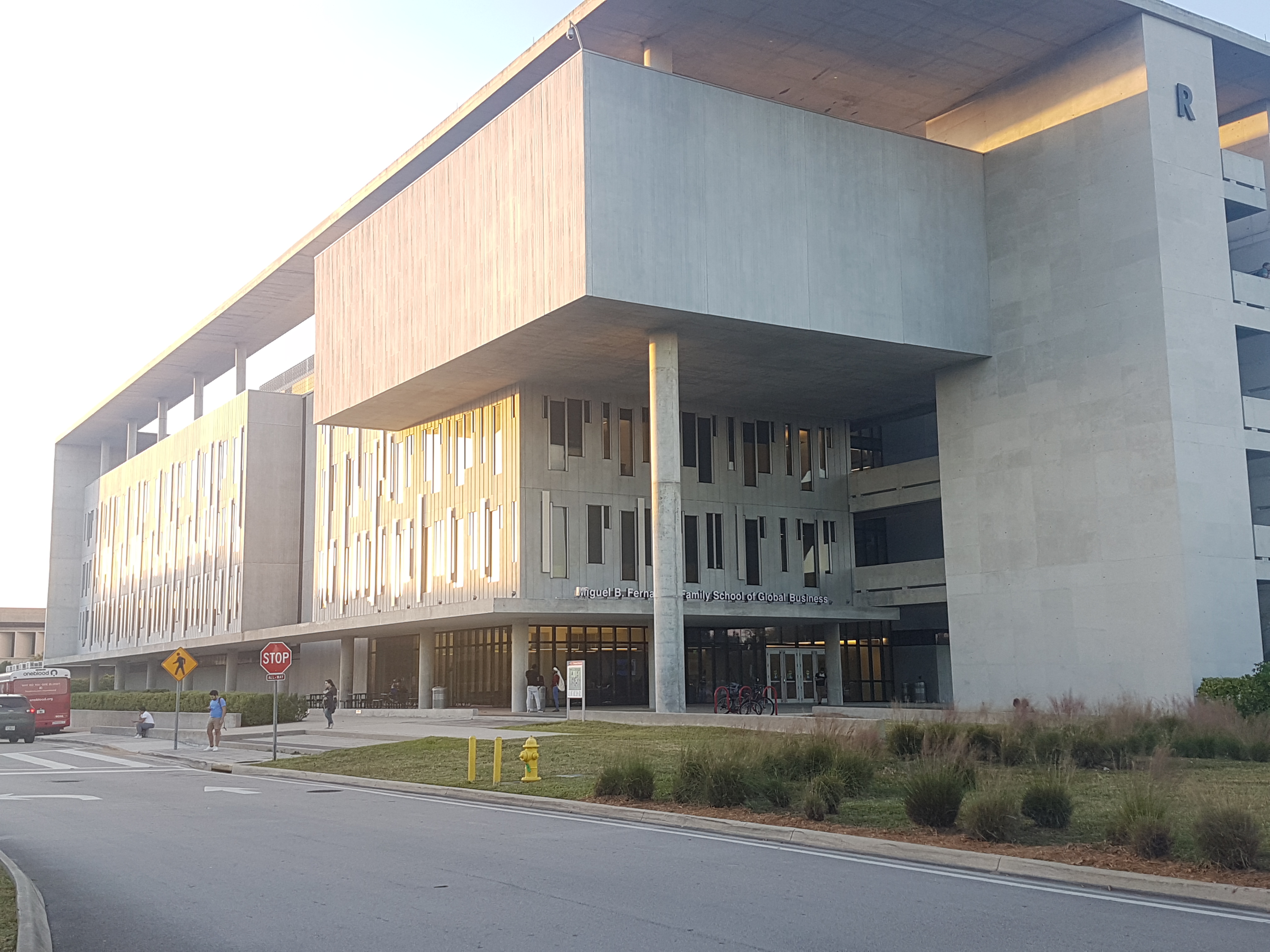 Large modern concrete and glass college building with campus road and landscaping in the foreground.