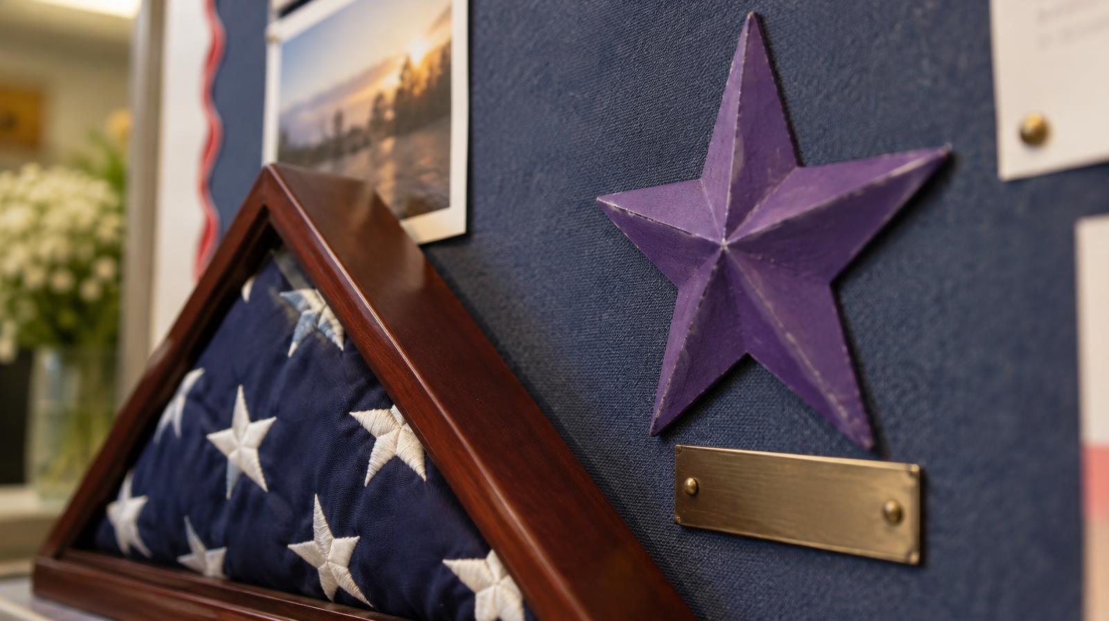 A purple star on a bulletin board next to a folded American flag and a nameplate.