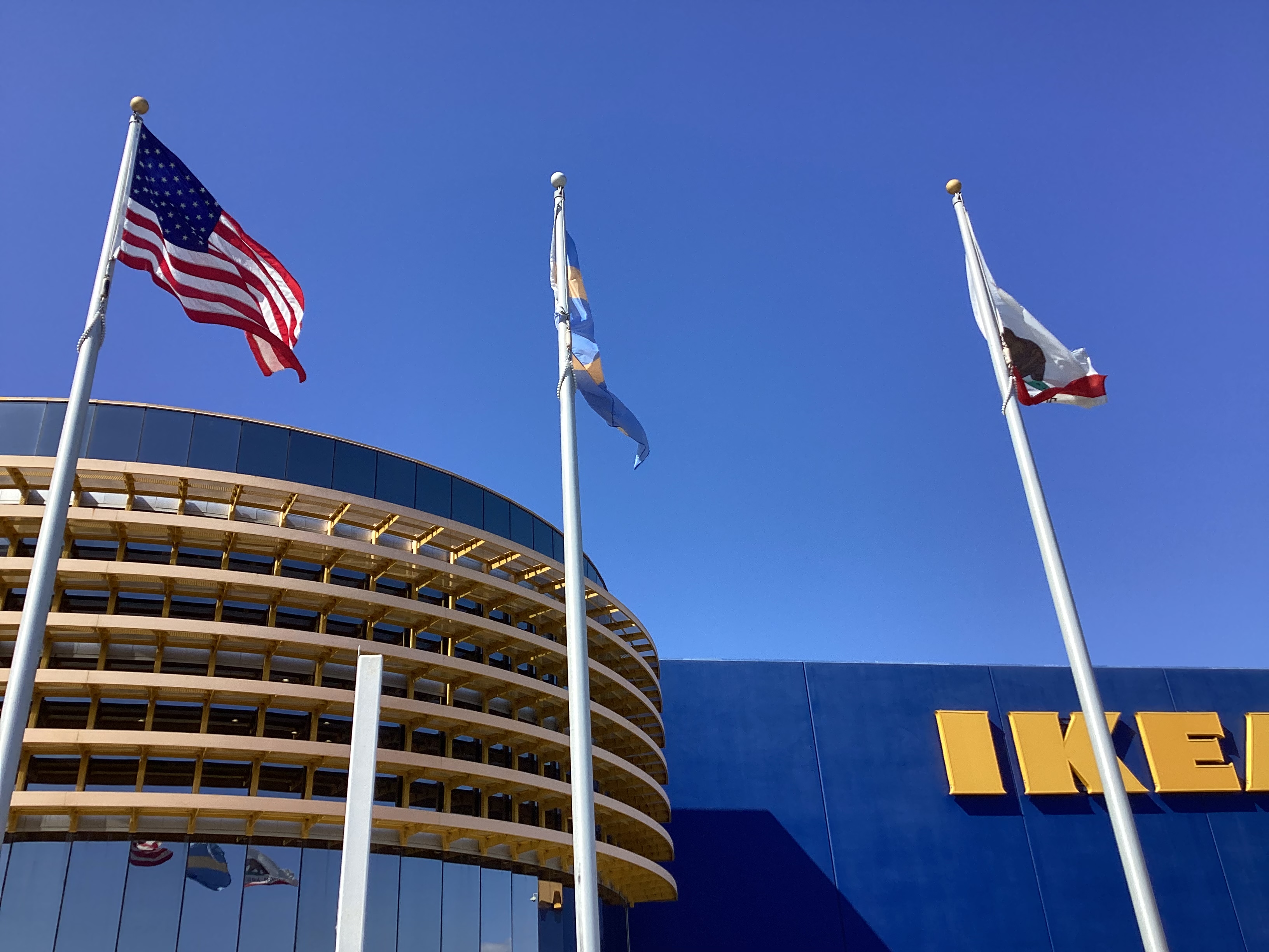 Exterior of an IKEA store with American and California flags flying on poles in front.