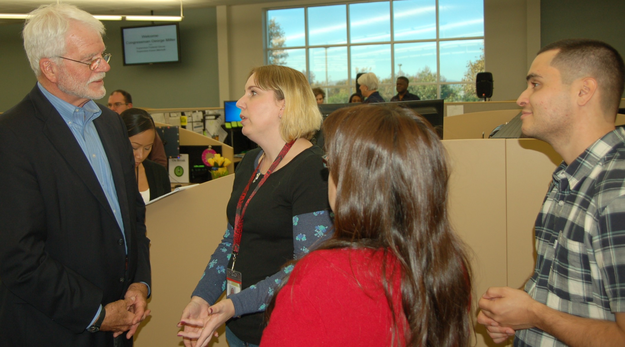 Group of adults conversing inside a call center office with workstations visible in the background.