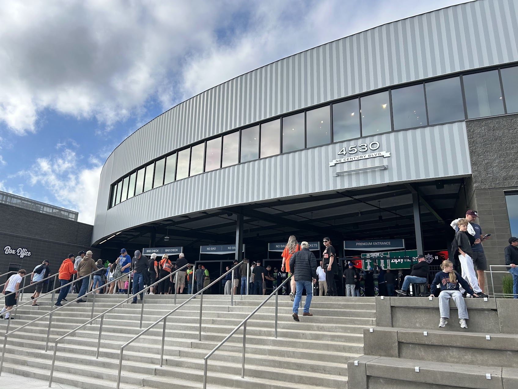 Crowds of fans walking up steps toward the entrance of a modern baseball stadium.