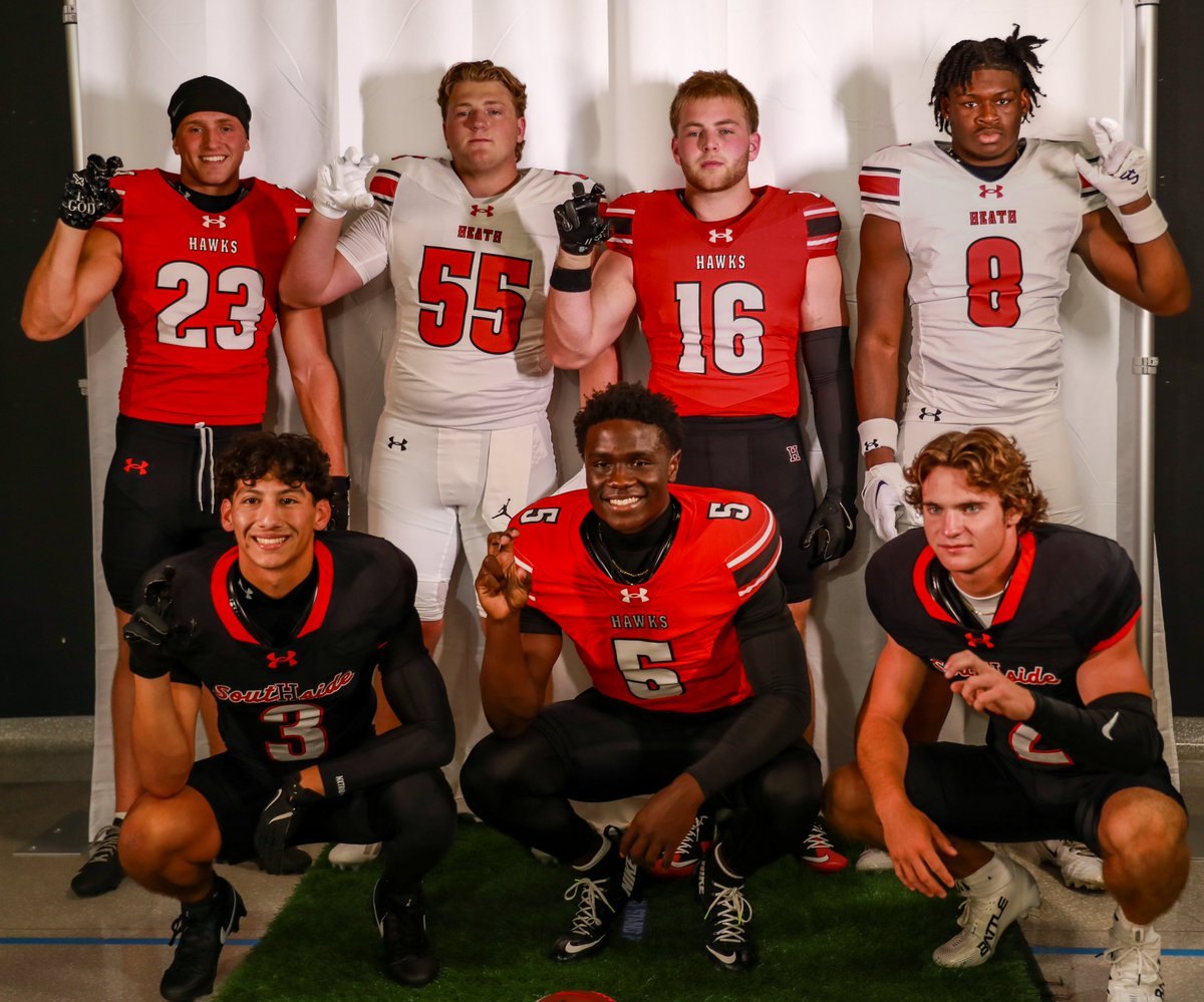 Seven football players in red and white Hawks uniforms pose together in a team facility.