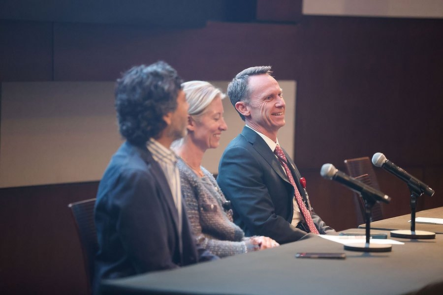 Three people seated at a long table with microphones at an indoor panel event.