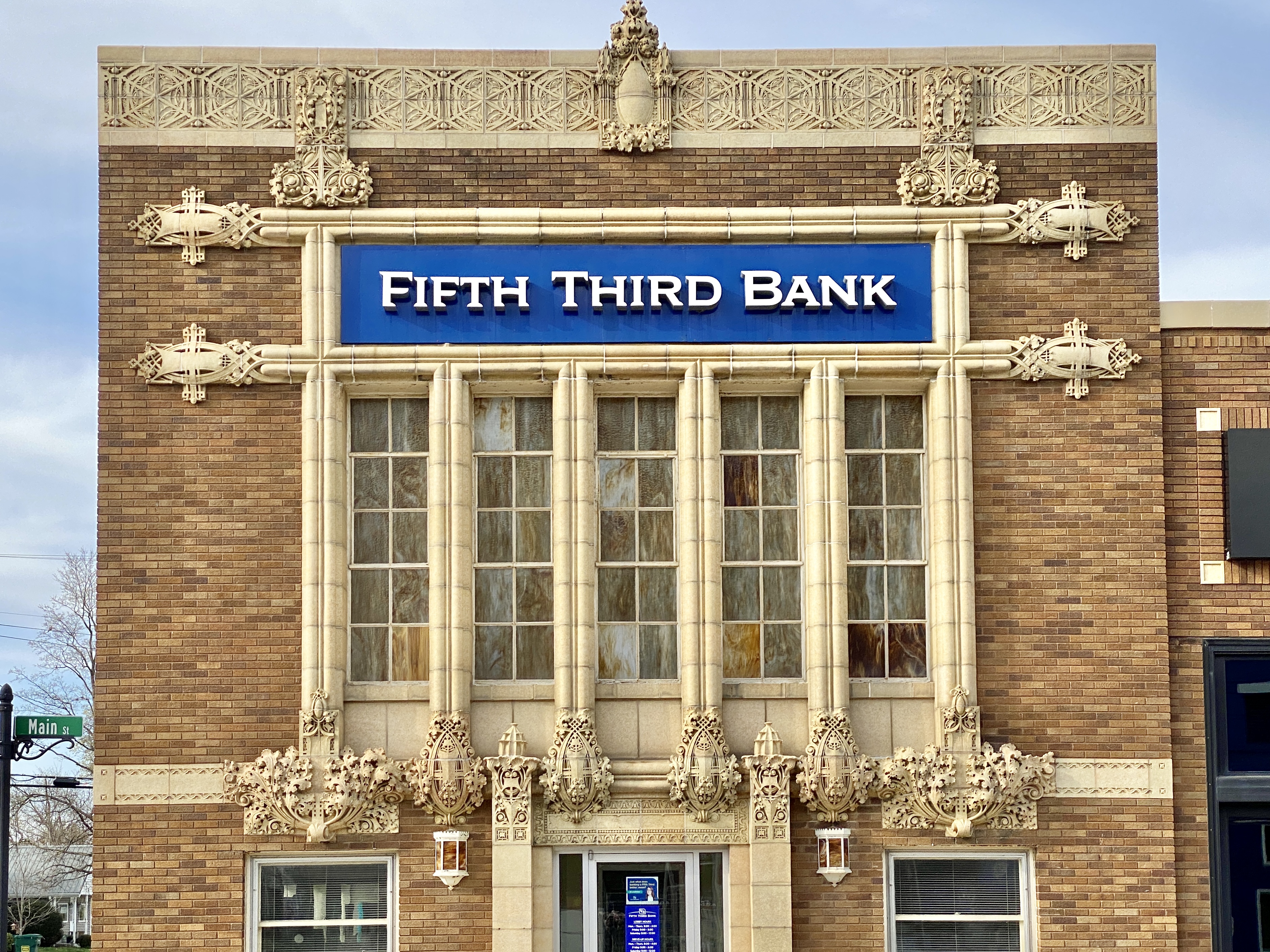 Close view of a historic brick bank facade with a blue Fifth Third Bank sign and ornate terra cotta trim.