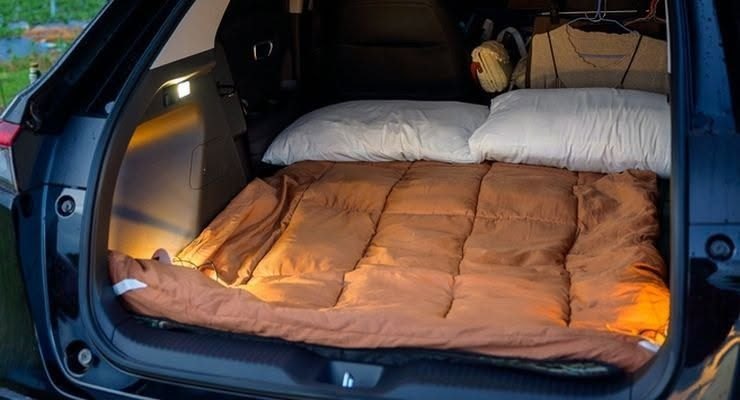 Brown comforter and white pillows arranged as a bed in the cargo area of a vehicle.