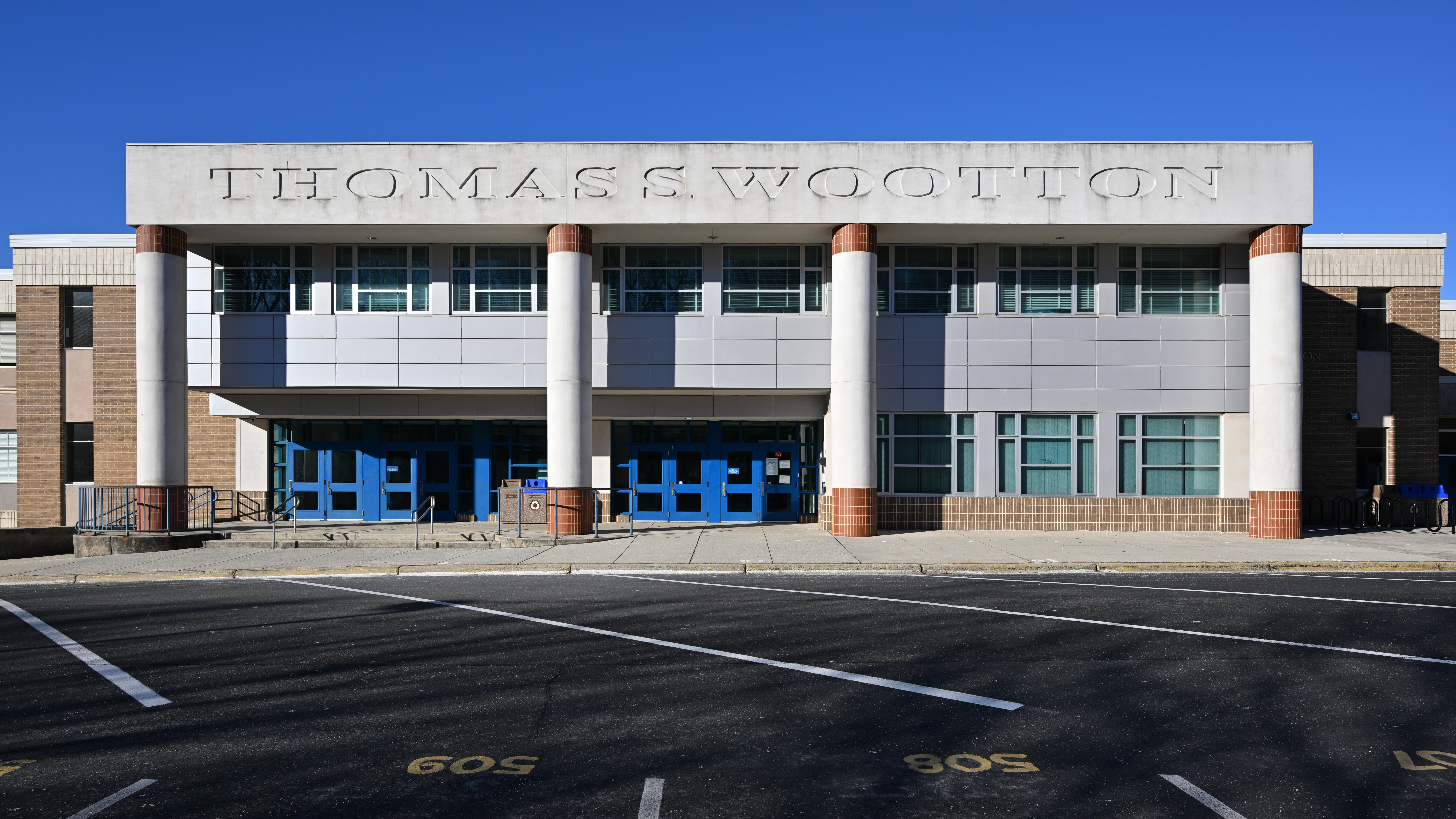 Front entrance of a modern school building with the name Thomas S. Wootton engraved above blue doors and white columns.