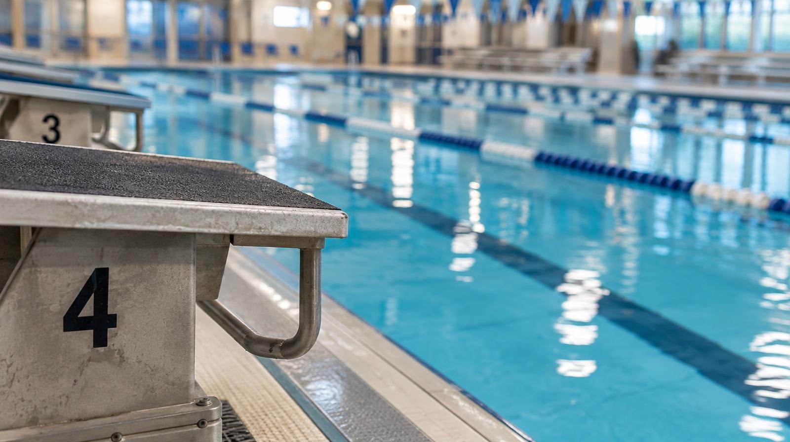 Empty indoor swimming pool with lane dividers and starting blocks under bright overhead lights.