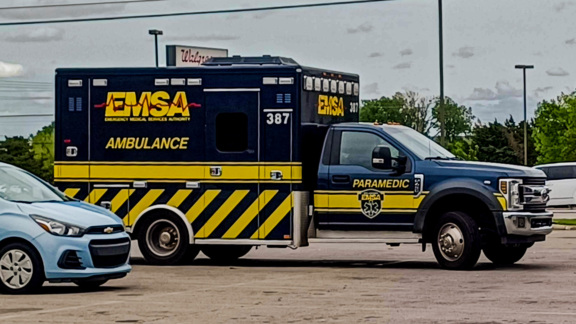 A dark navy blue EMSA ambulance and paramedic truck parked in a lot.