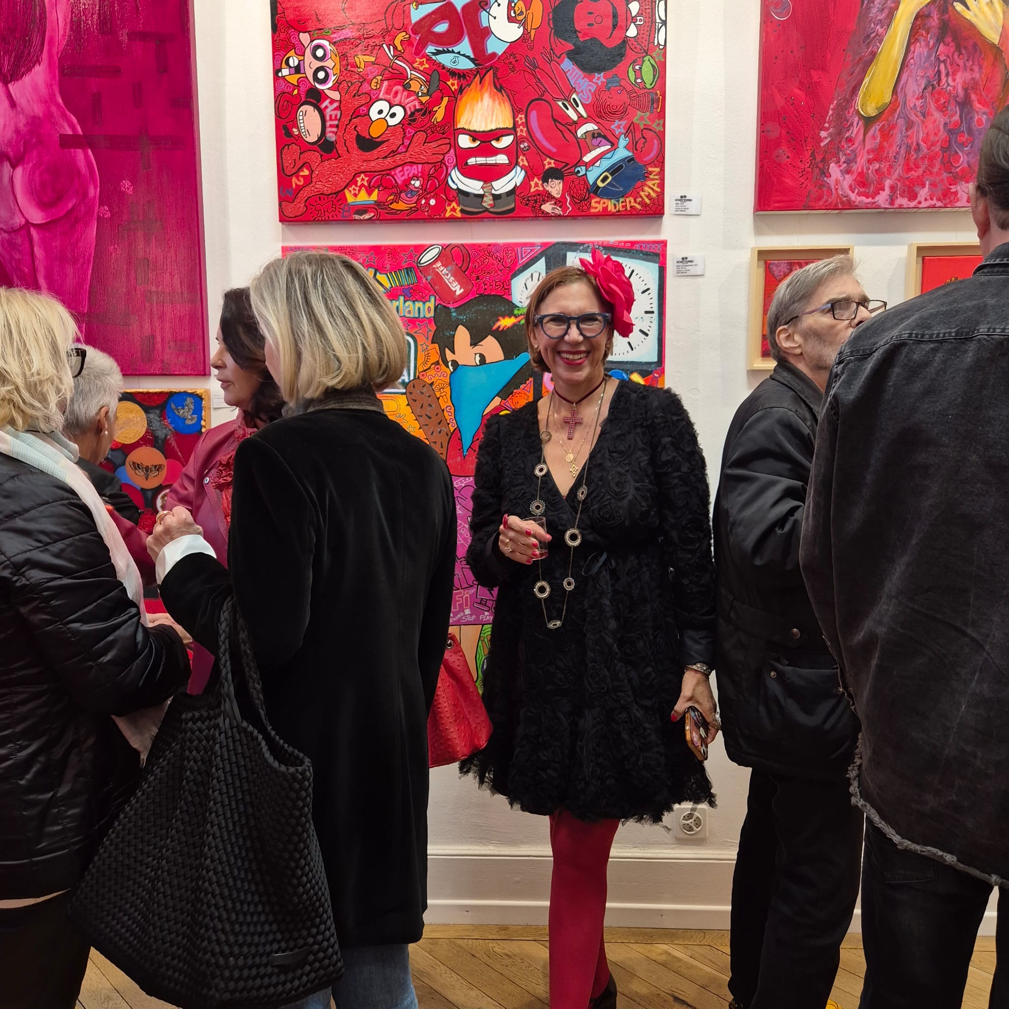 Visitors gathered and talking at an art gallery opening with colorful paintings on white walls.