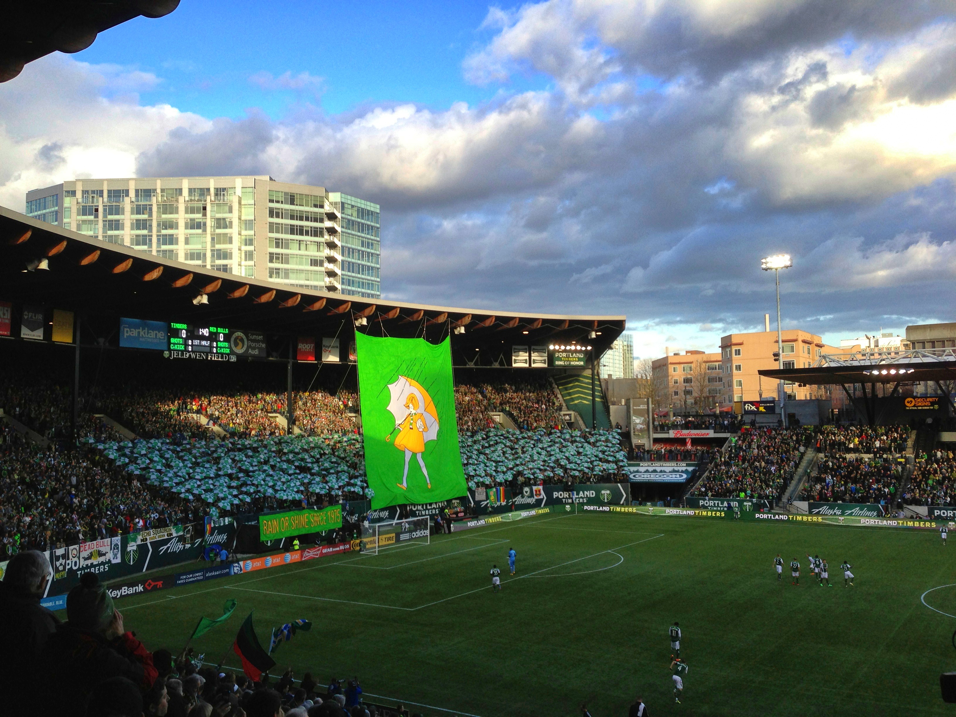 Soccer stadium filled with fans and a large green tifo banner in the supporters' section.