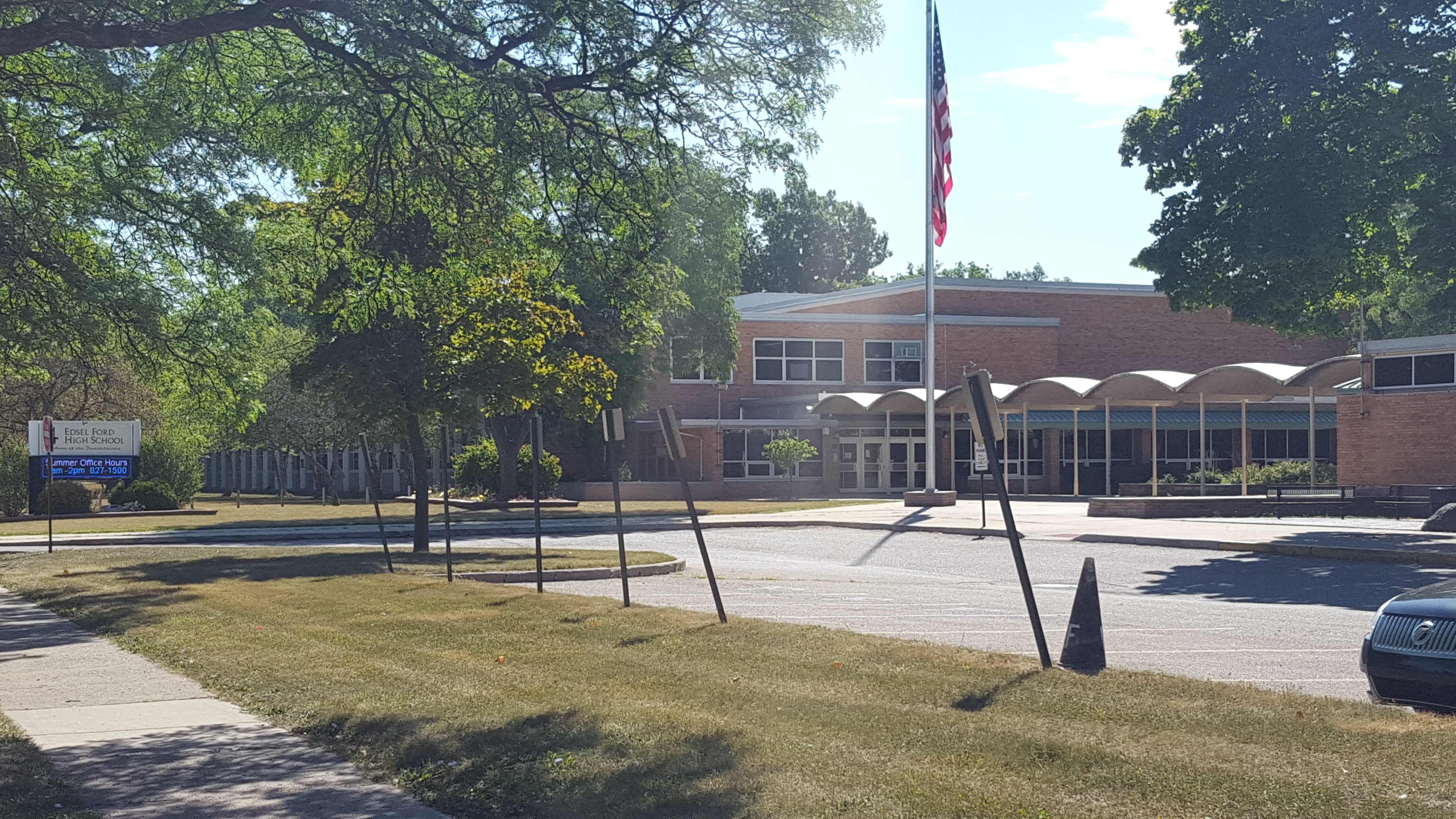 Brick school building with a flagpole and covered entrance surrounded by trees.