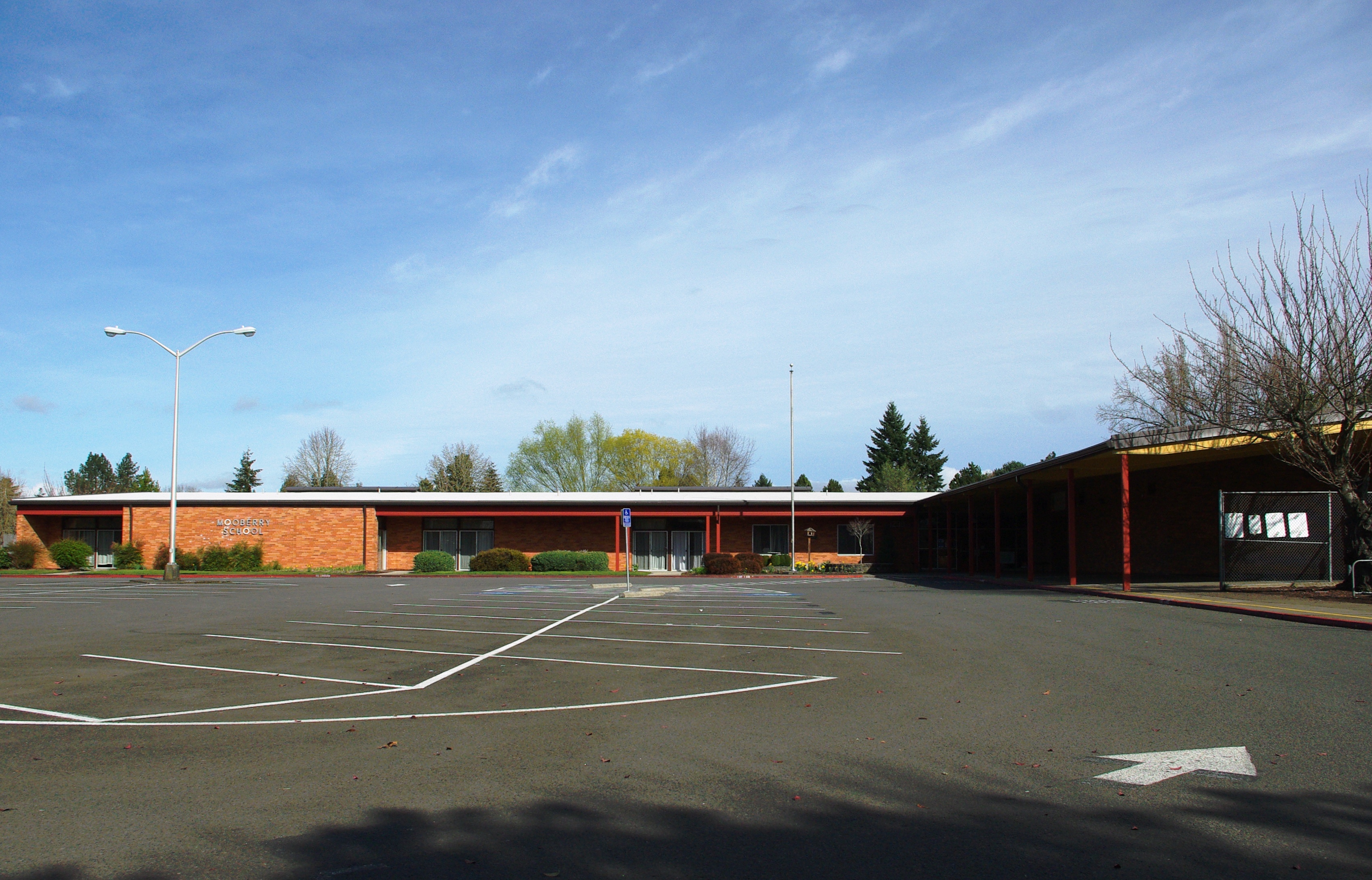 Single-story brick elementary school building with red trim and a large parking lot in front.