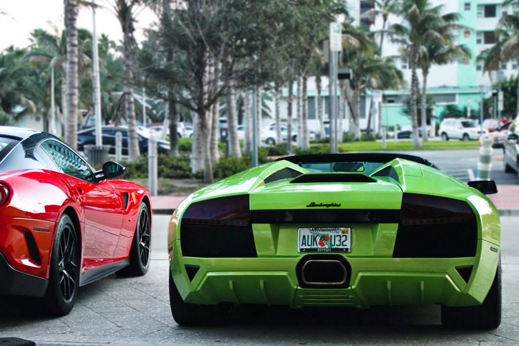 Rear view of a lime-green Lamborghini parked beside a red Ferrari outdoors.