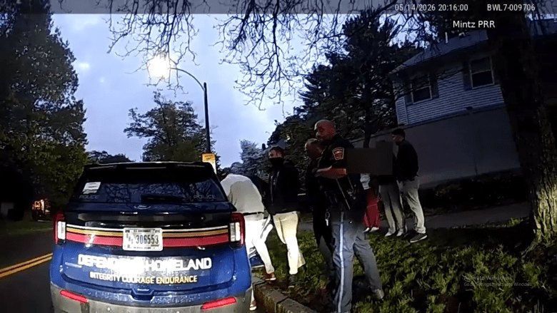 Body camera screenshot showing people in dark clothing near a blue SUV at dusk.