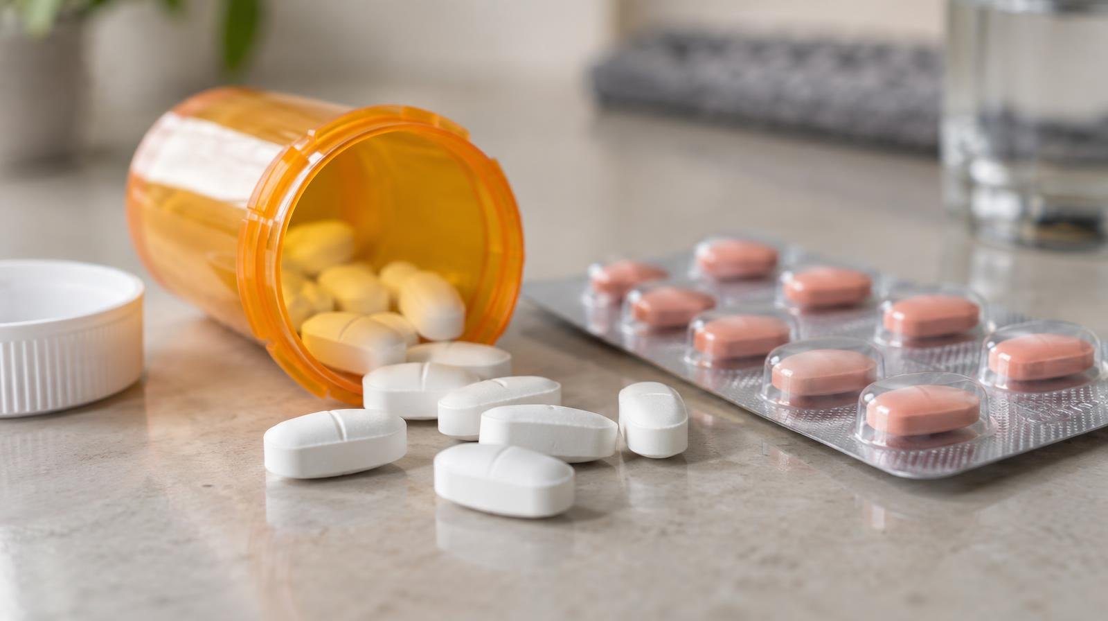 Orange prescription pill bottle tipped over with white tablets spilling out beside a blister pack.