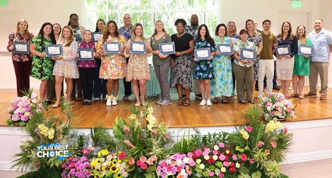 Group of people standing on a decorated stage holding framed certificates at an awards ceremony.