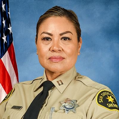Woman in San Diego County Sheriff's captain uniform posed before an American flag.