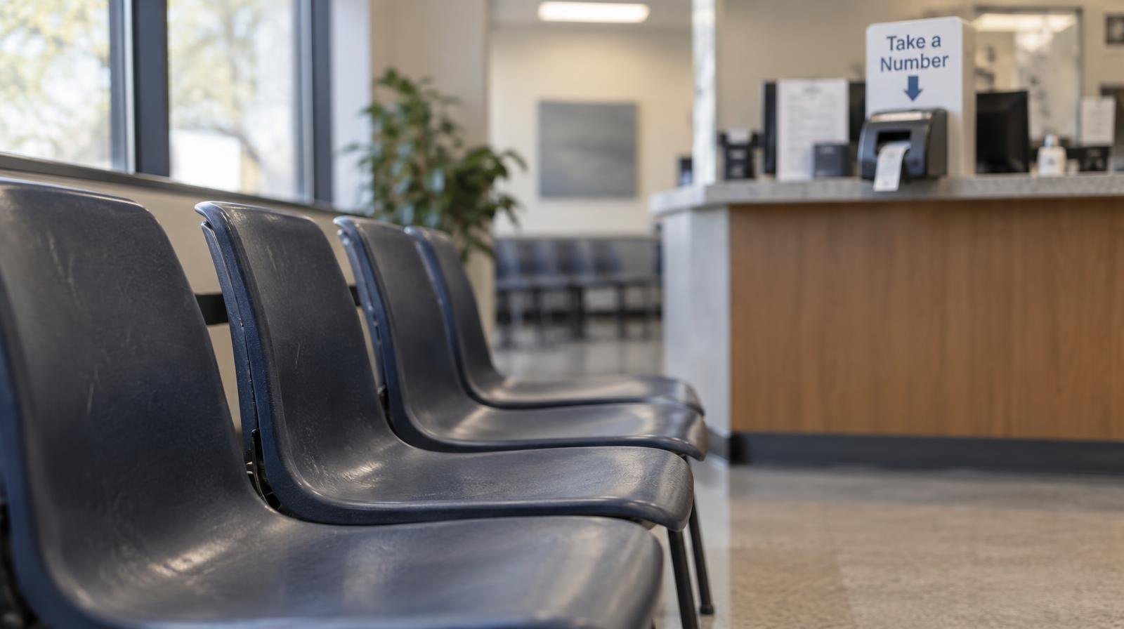 Rows of empty plastic chairs in a fluorescent-lit government waiting room.