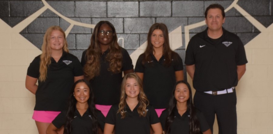 Seven people in matching black polo shirts pose in two rows for a team photo.