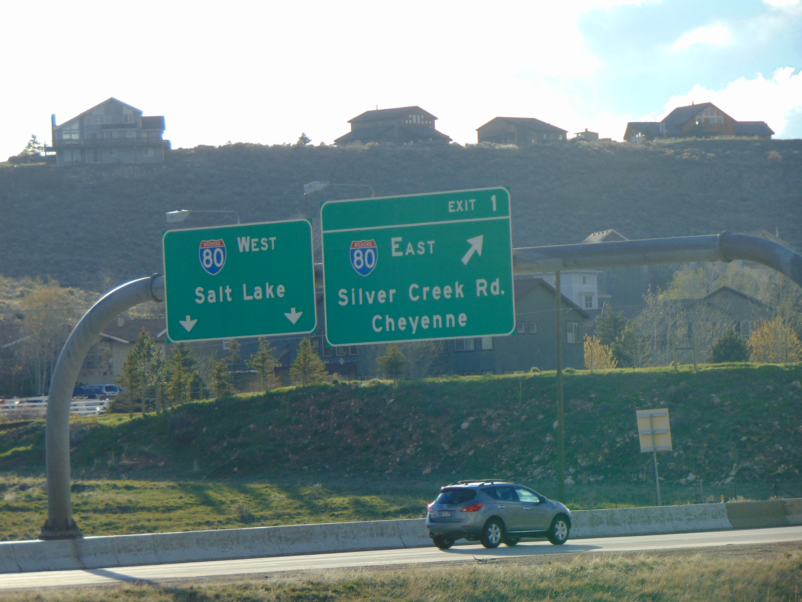Overhead highway gantry signs on Interstate 80 in Summit County, Utah, with homes on a hillside behind.